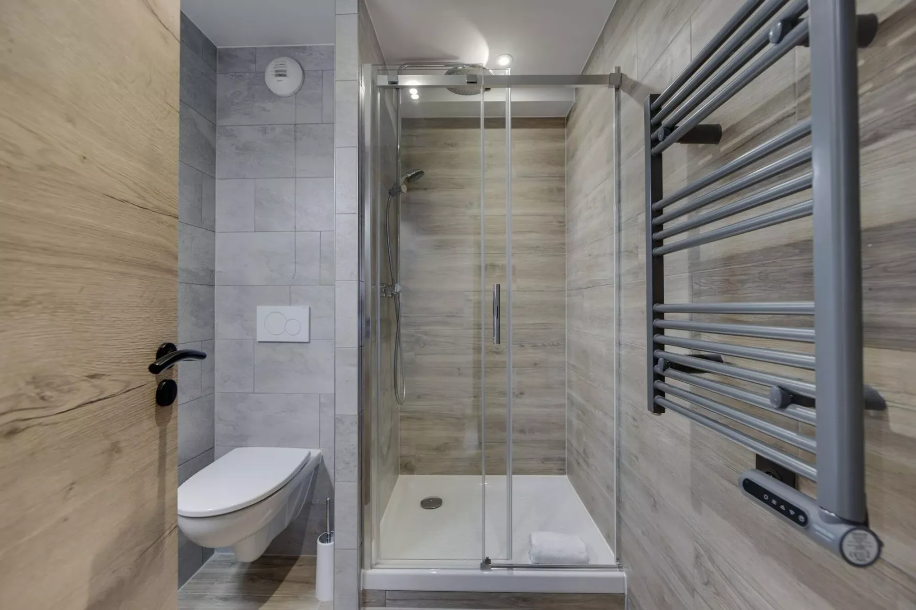 A tiled bathroom with a glass shower, wall-mounted toilet, and heated towel rail.