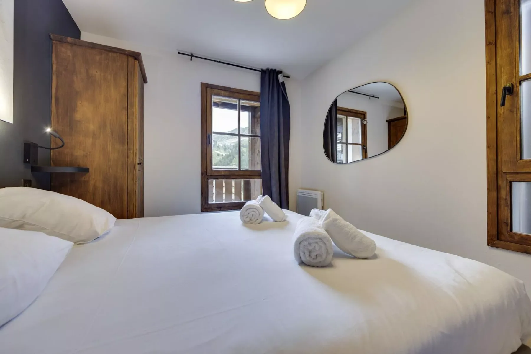 A bedroom with a neatly made bed and wooden-framed windows.