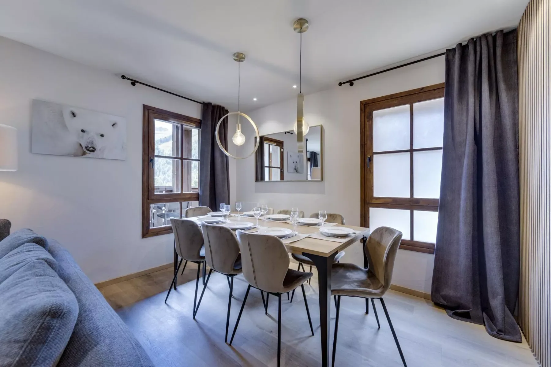 Un comedor con la mesa puesta junto a ventanas altas y cortinas oscuras.