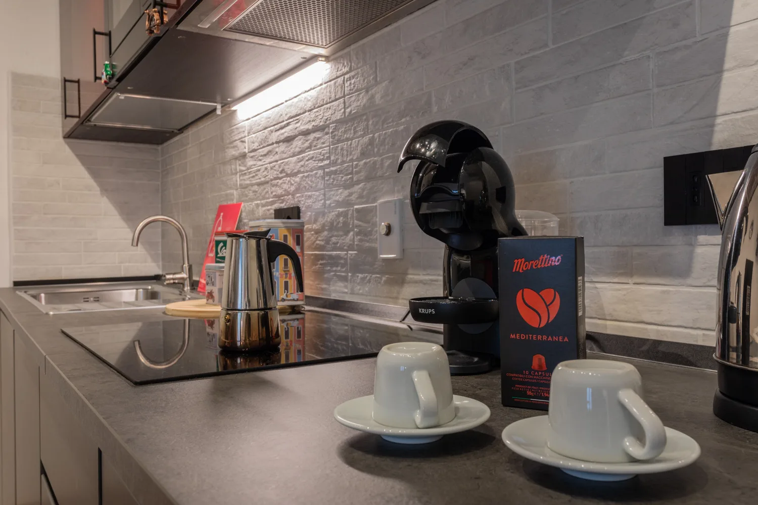 A compact kitchen counter with a coffee machine, kettle, and cups.