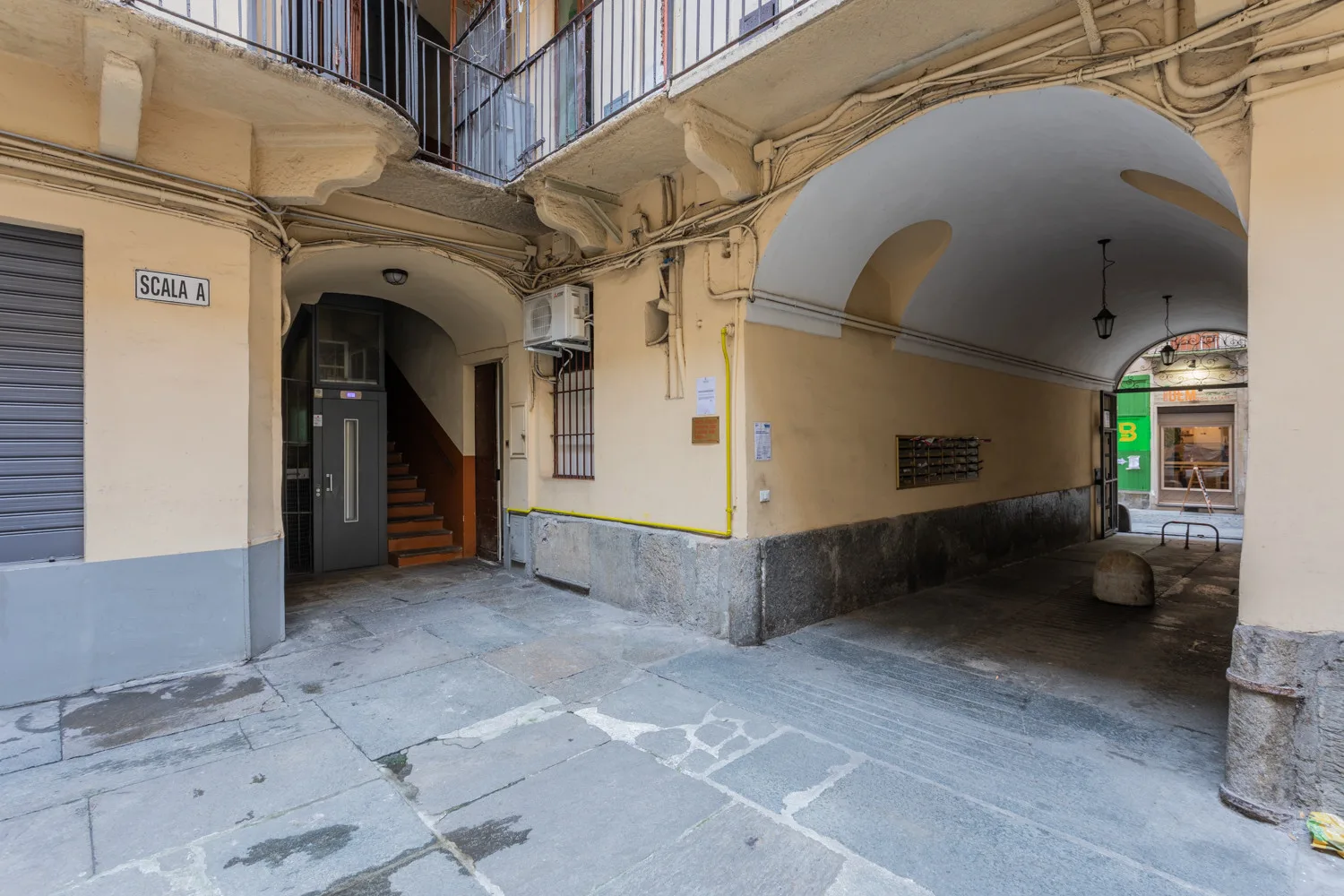 An arched passageway opens onto a paved courtyard, with a stairwell beside it.