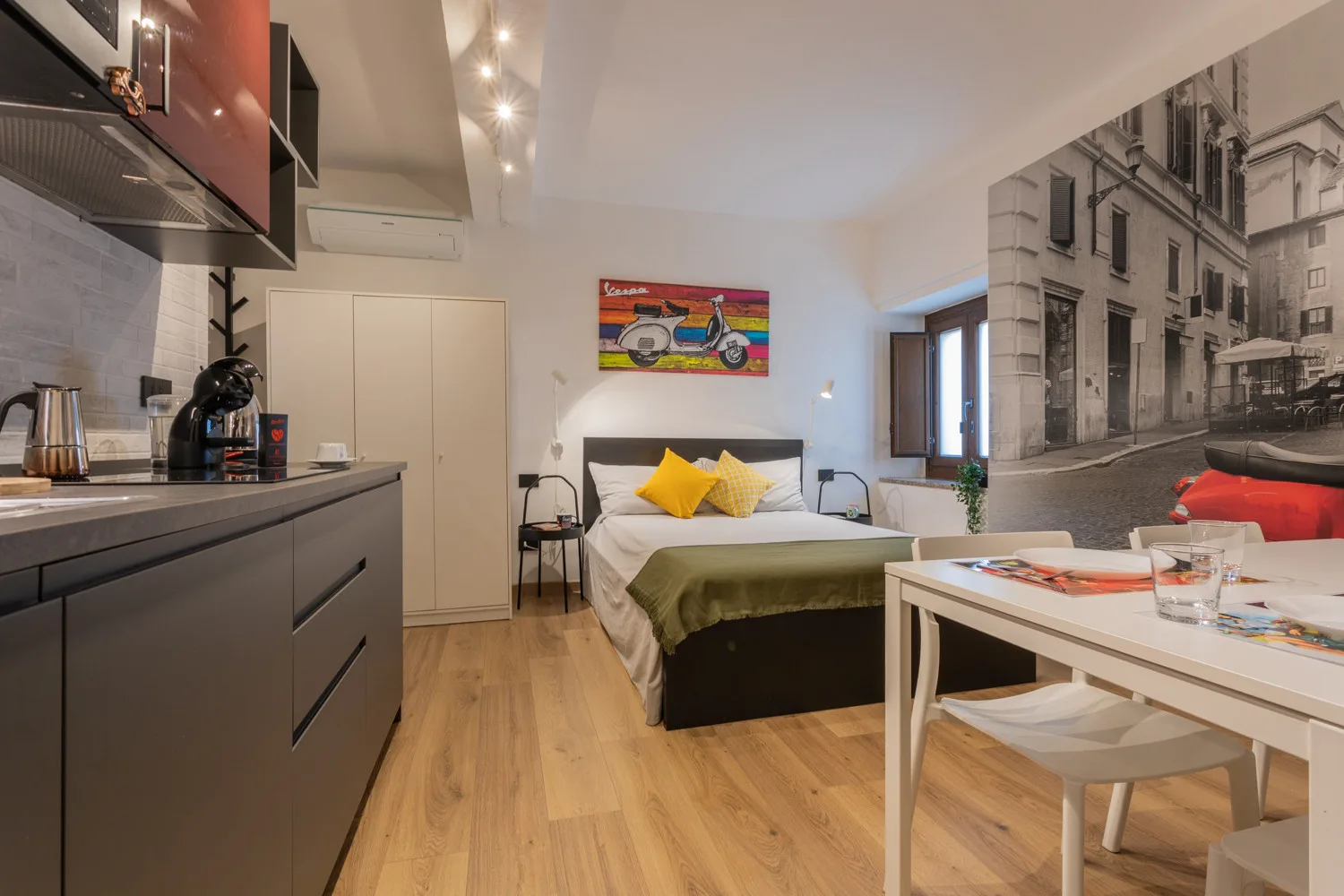 A compact bedroom with a bed, kitchenette, and dining table.