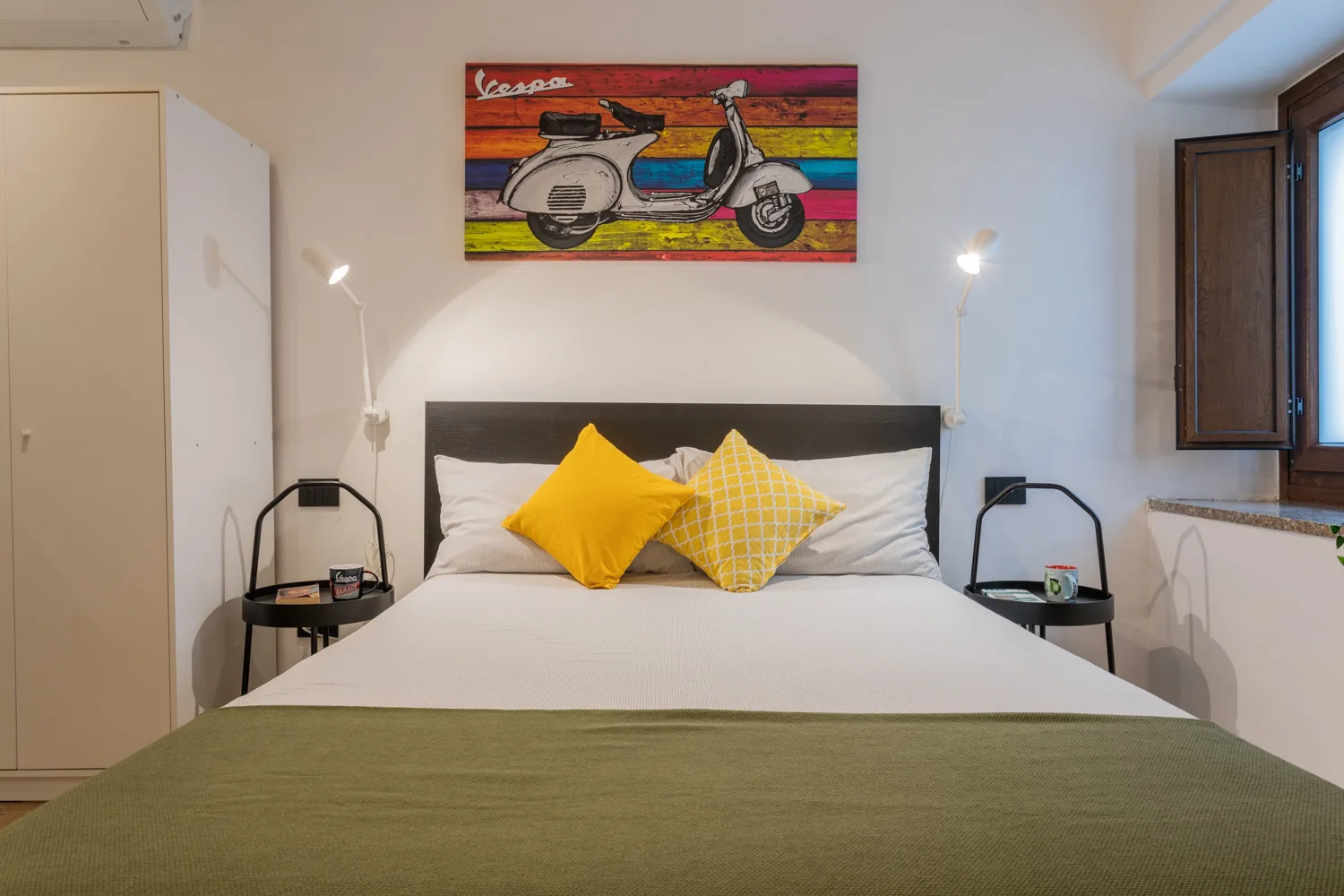 A bedroom with a neatly made bed and colorful scooter artwork above the headboard.