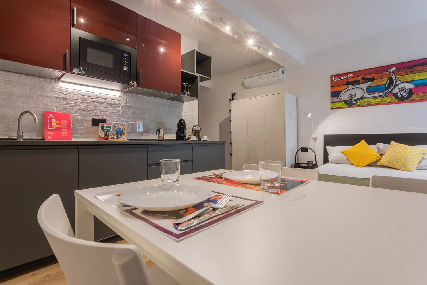 A compact kitchen and dining area opens onto a seating space with colorful cushions.