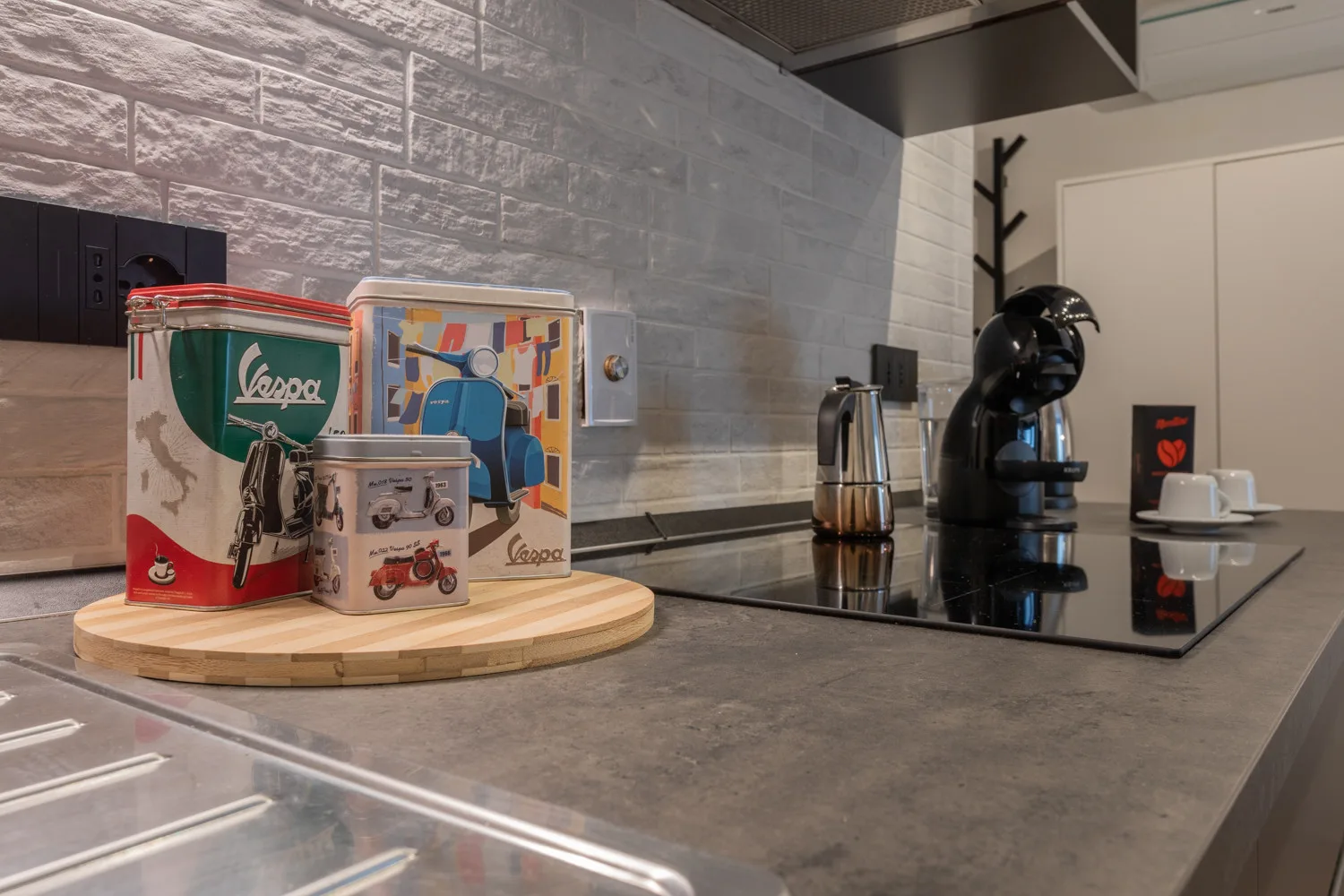 A modern kitchen counter displays decorative tins beside a stovetop and coffee maker.