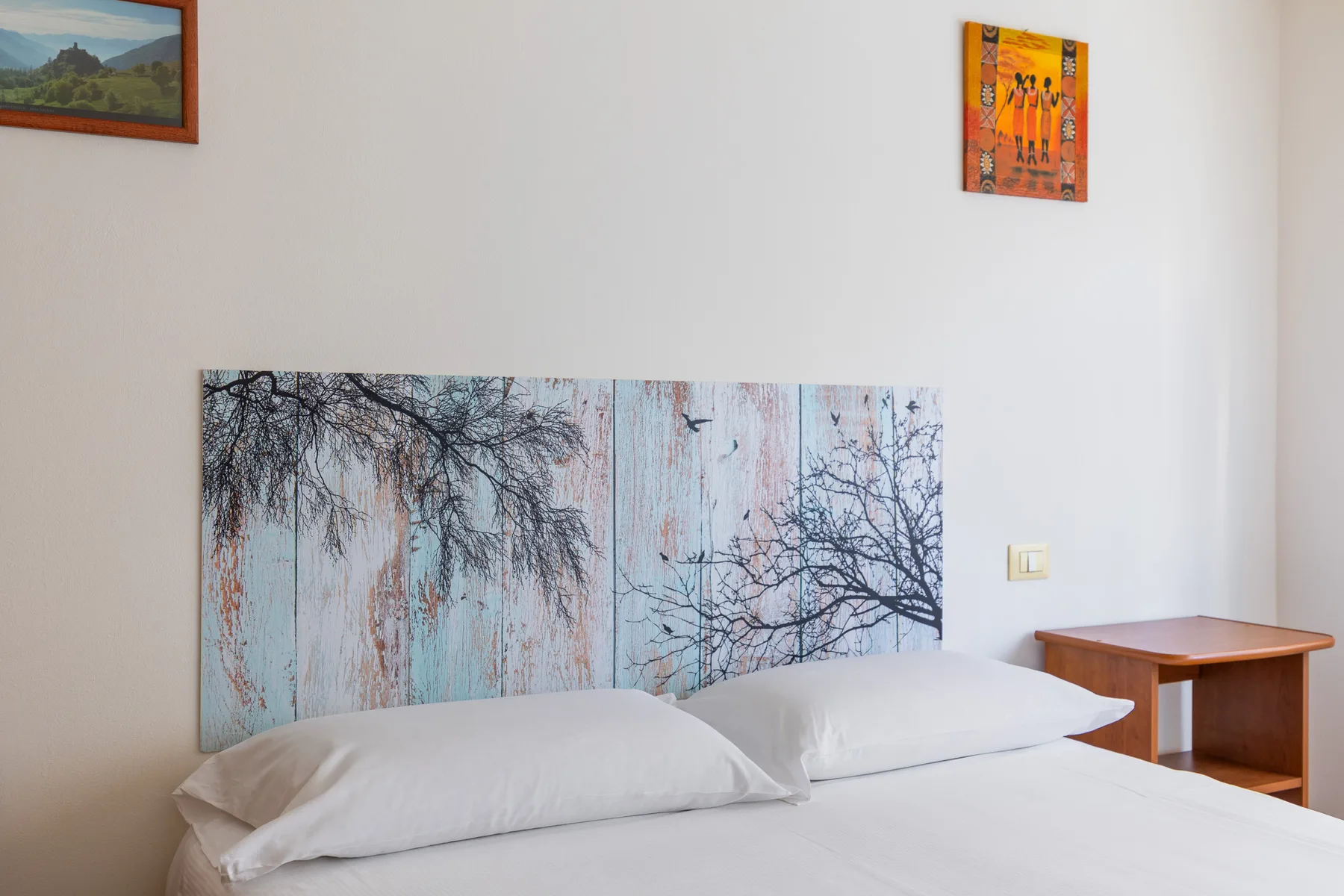 A bedroom with a bed beneath a large tree-themed wall artwork.
