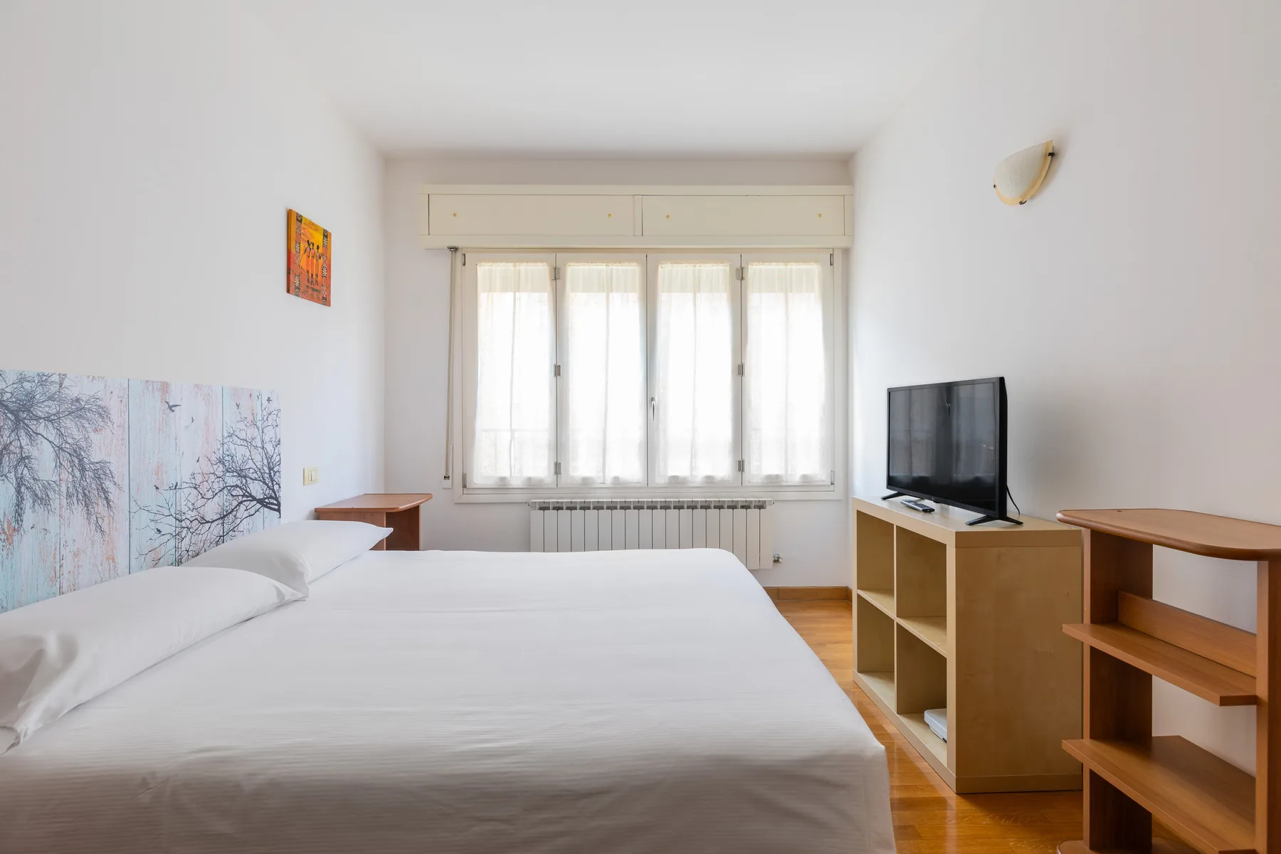 A bedroom with a neatly made bed, a window, and a television on a cabinet.