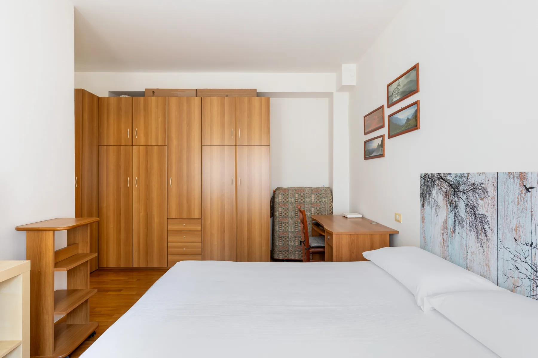 A bedroom with a bed, wooden wardrobe, and desk.