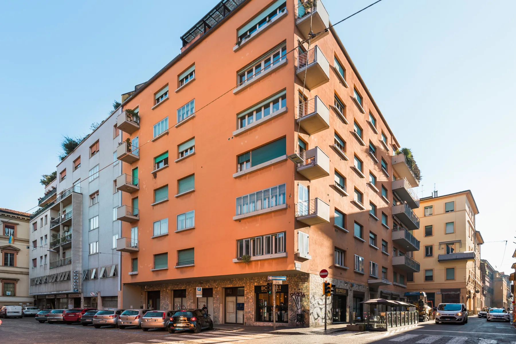 An orange apartment building stands on a city street beside neighboring buildings.