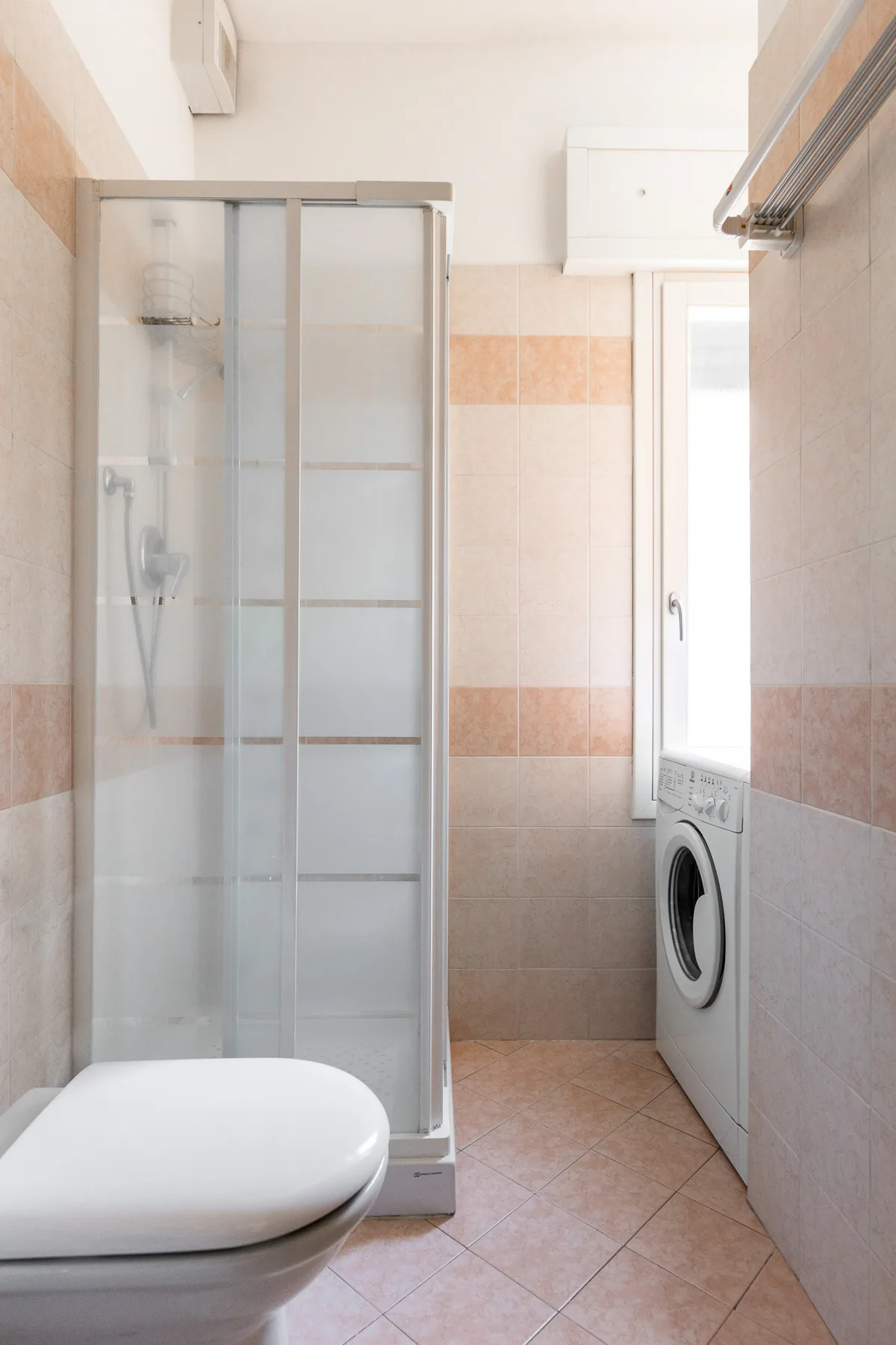 A tiled bathroom with a glass shower, toilet, and washing machine.
