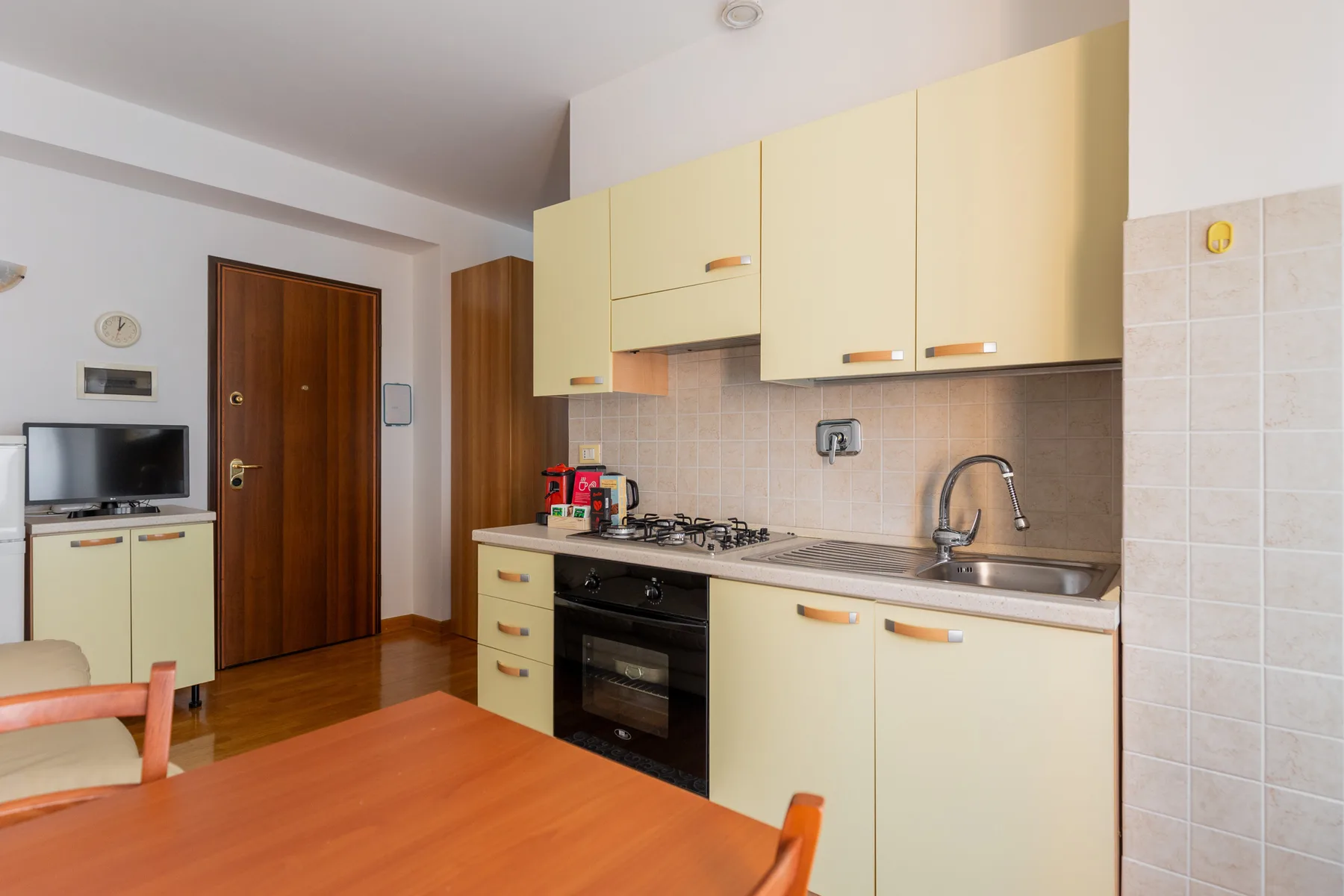 A kitchen with pale cabinets, a cooking range, and a dining table.