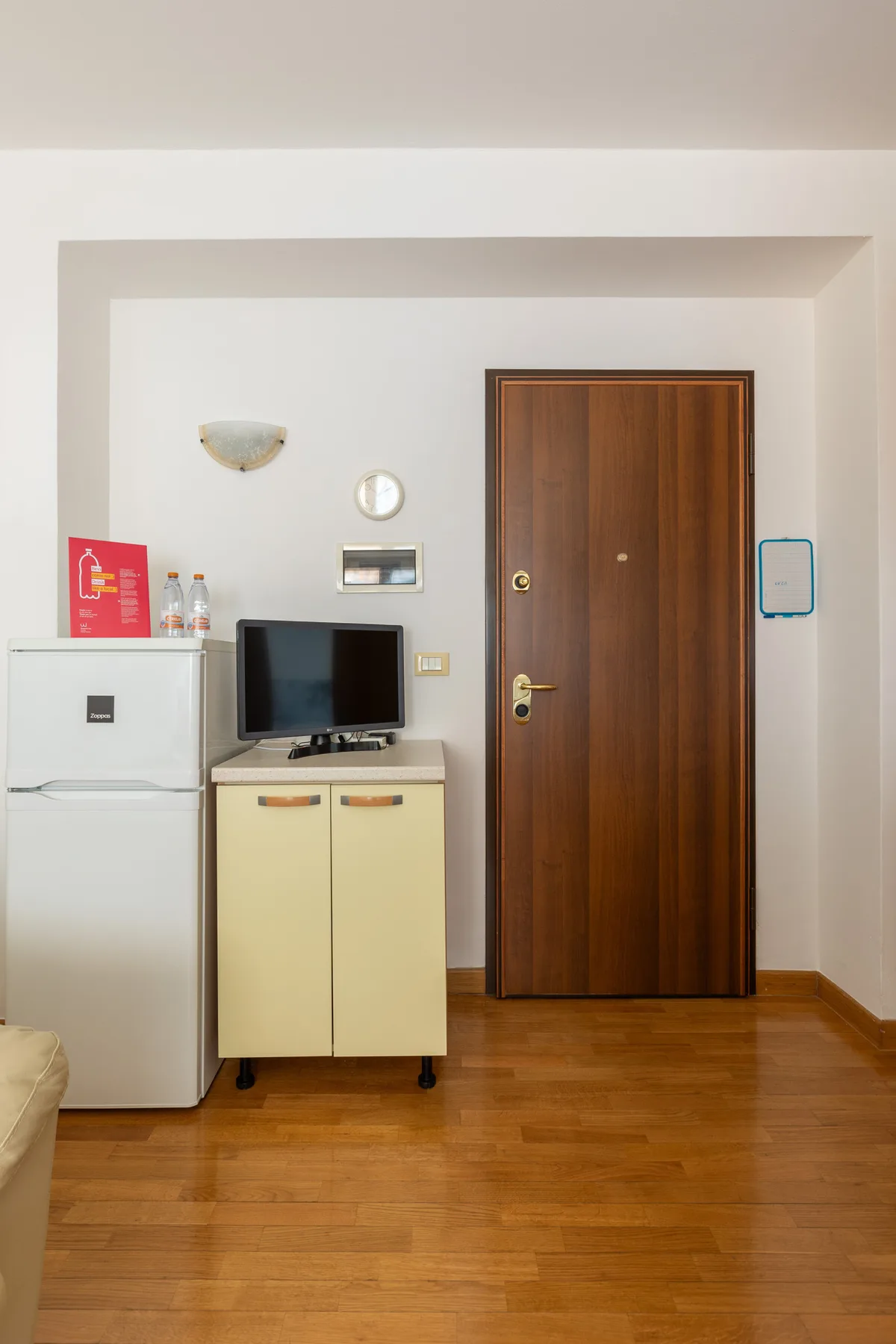 A room entry area with a wooden door, refrigerator, and television on a cabinet.