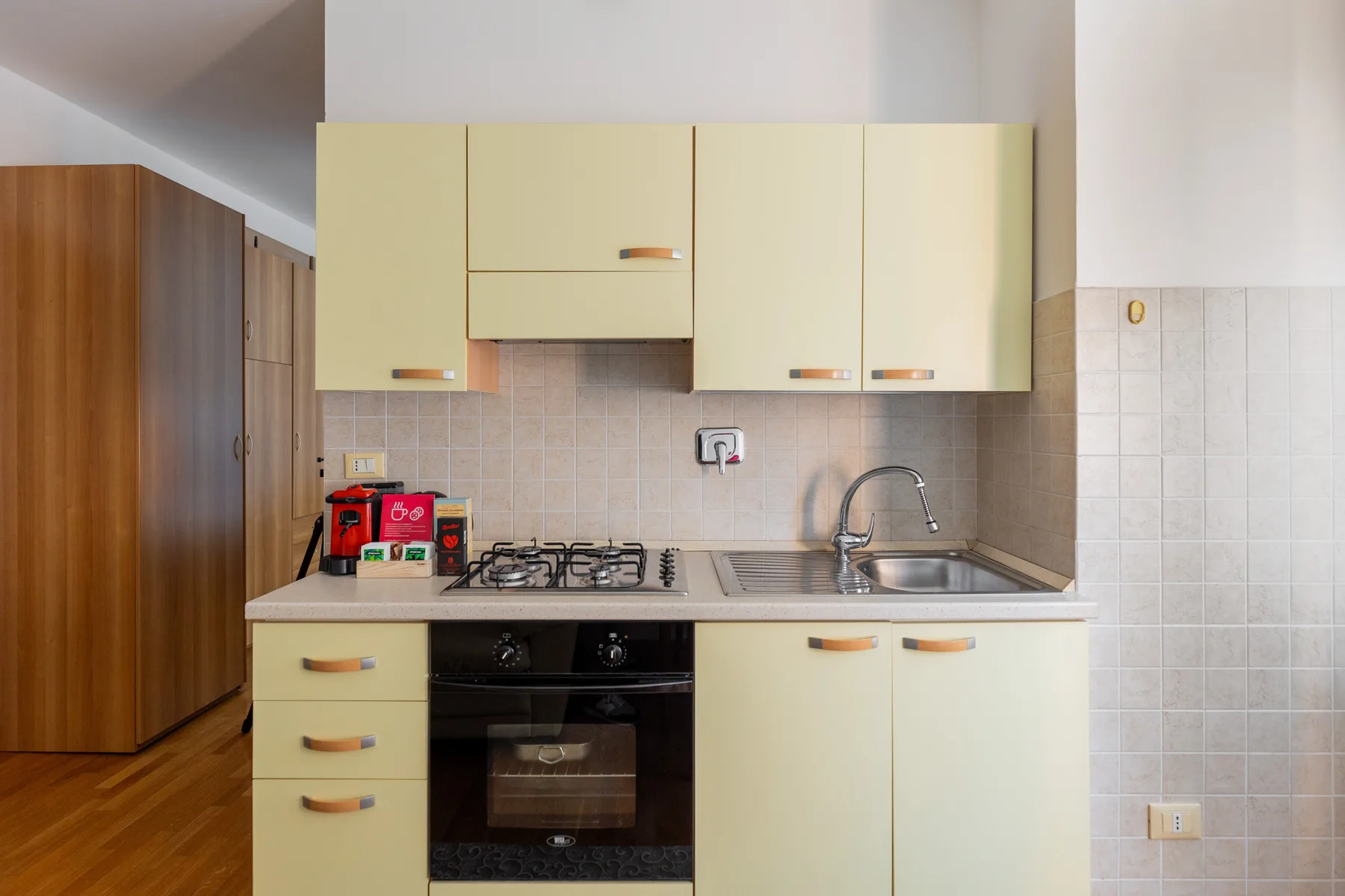 A kitchen with pale cabinets, a cooktop, and a sink.