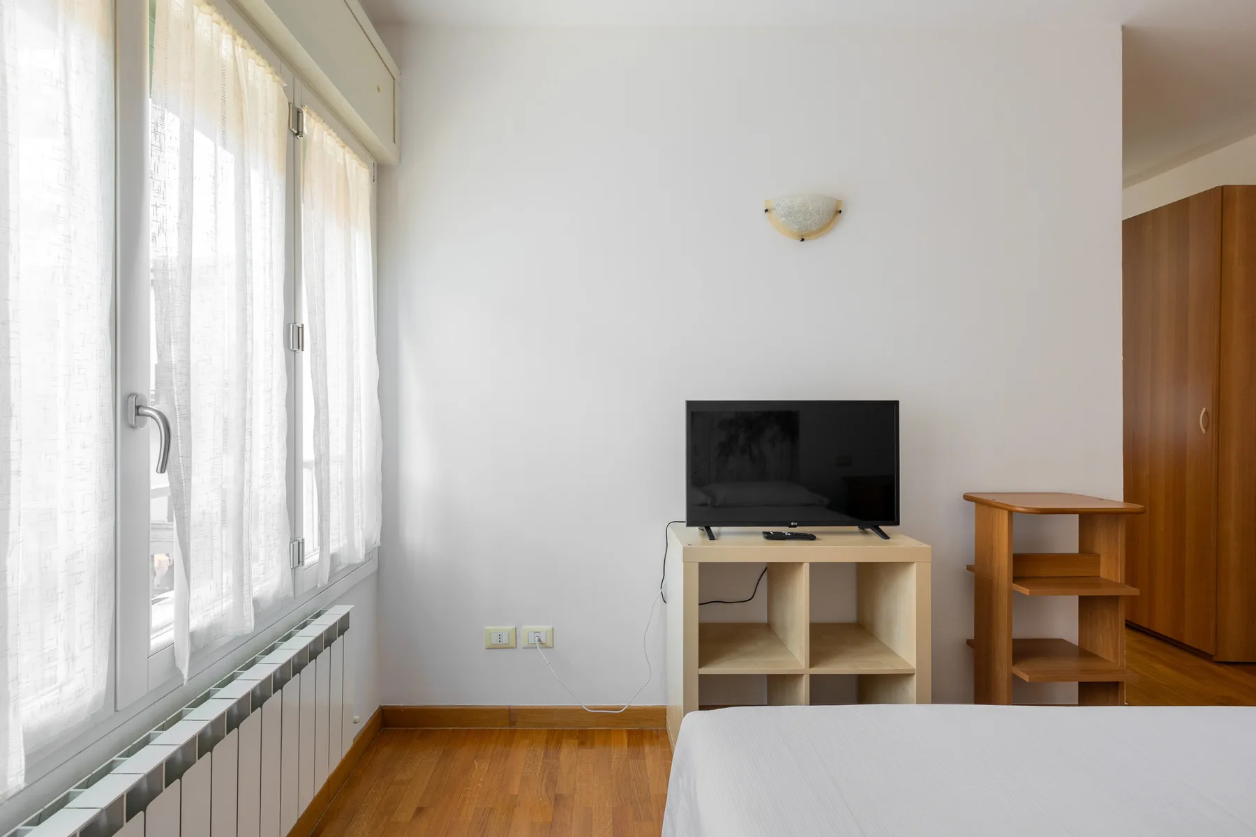 A bright bedroom with a television on a low stand beside the window.