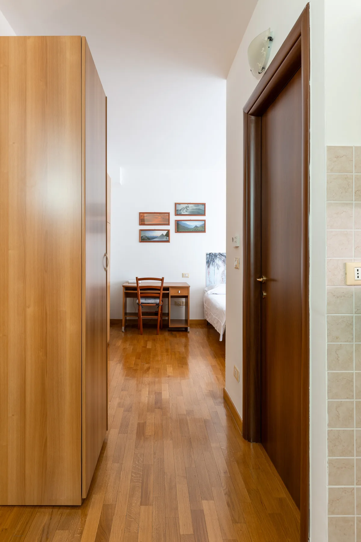 A narrow bedroom hallway leads to a desk and bed, with a wardrobe along the wall.
