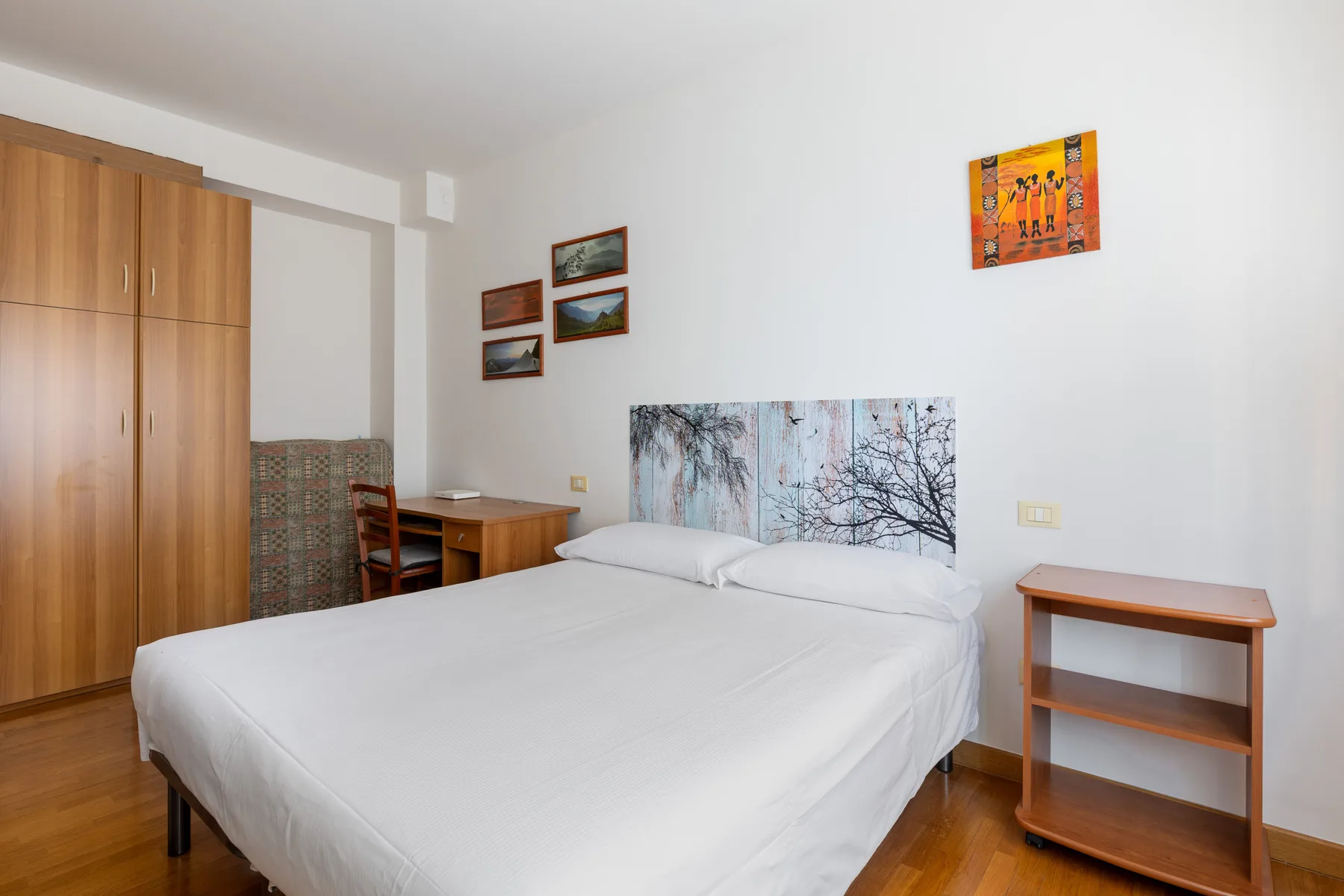A bedroom with a neatly made bed, wooden wardrobes, and a small bedside table.