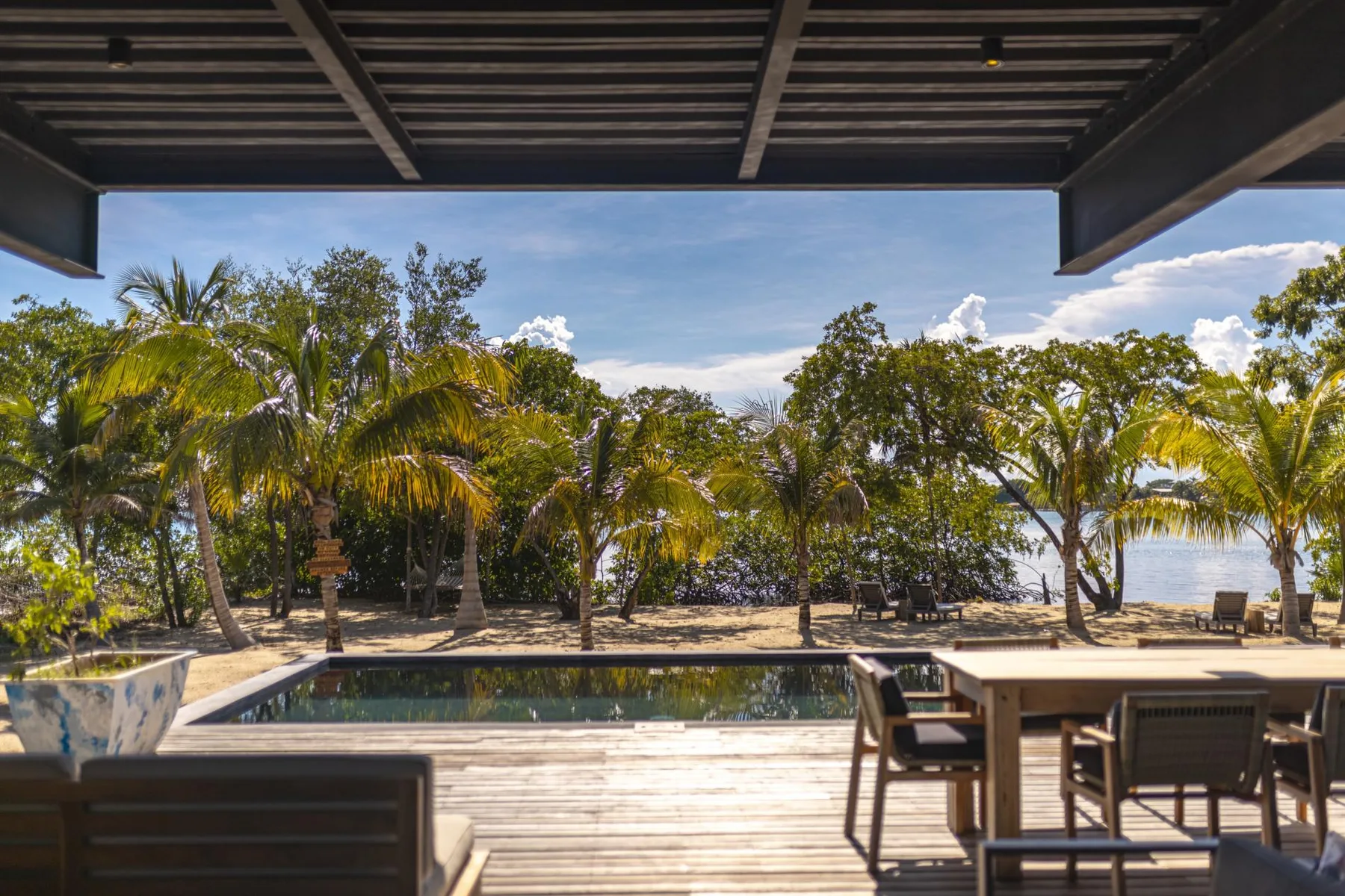 A poolside patio with outdoor seating overlooks palm trees and a landscaped garden.