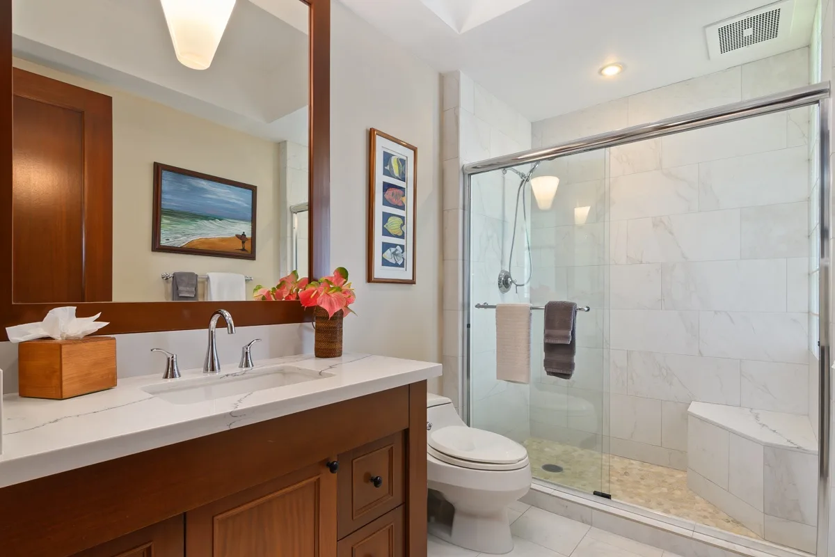 A bright bathroom with a vanity, toilet, and glass shower.