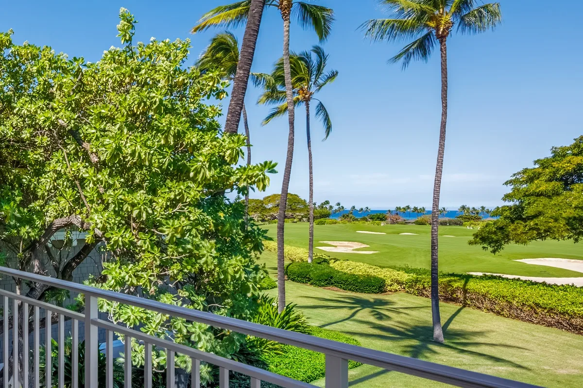 A tropical golf course stretches toward the ocean beyond a balcony railing.