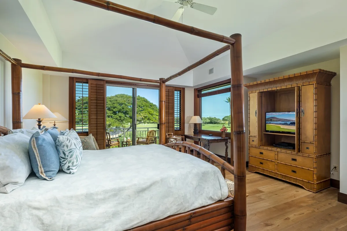 A bedroom with a large bed, wooden furnishings, and windows overlooking greenery.
