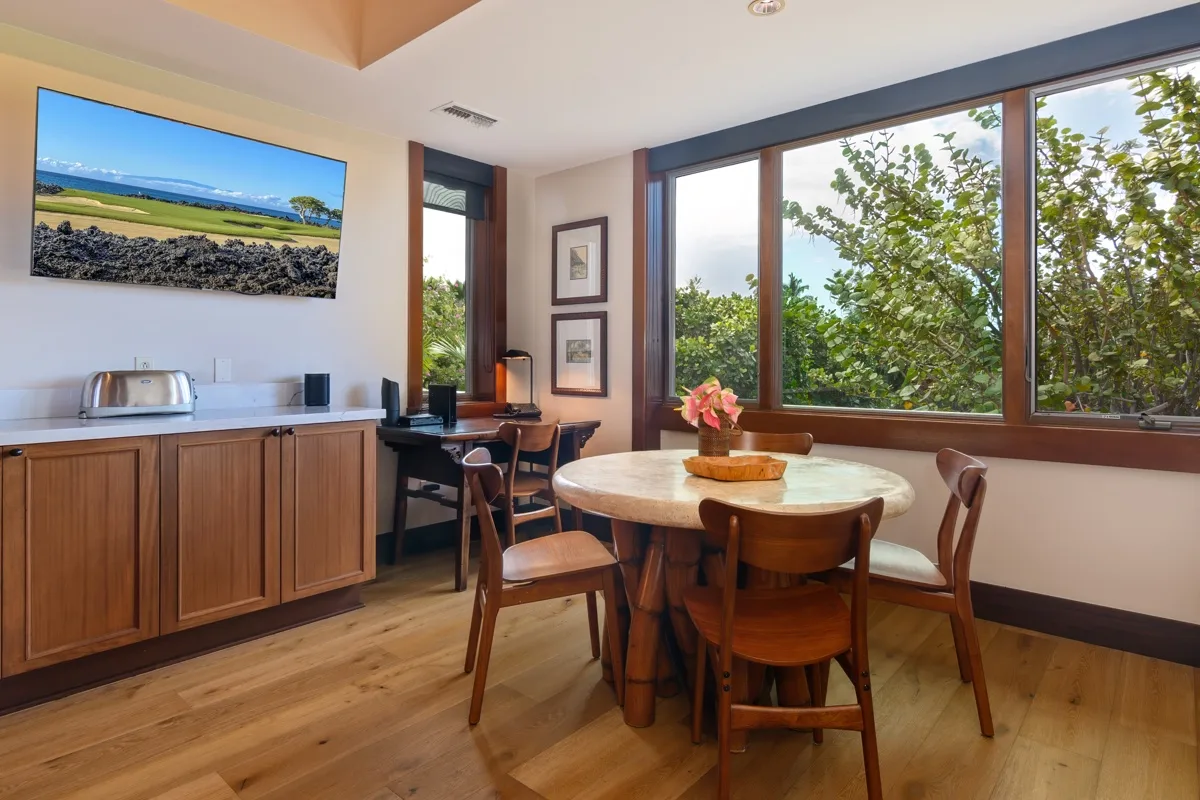 A dining area with a round table and large windows overlooking leafy trees.