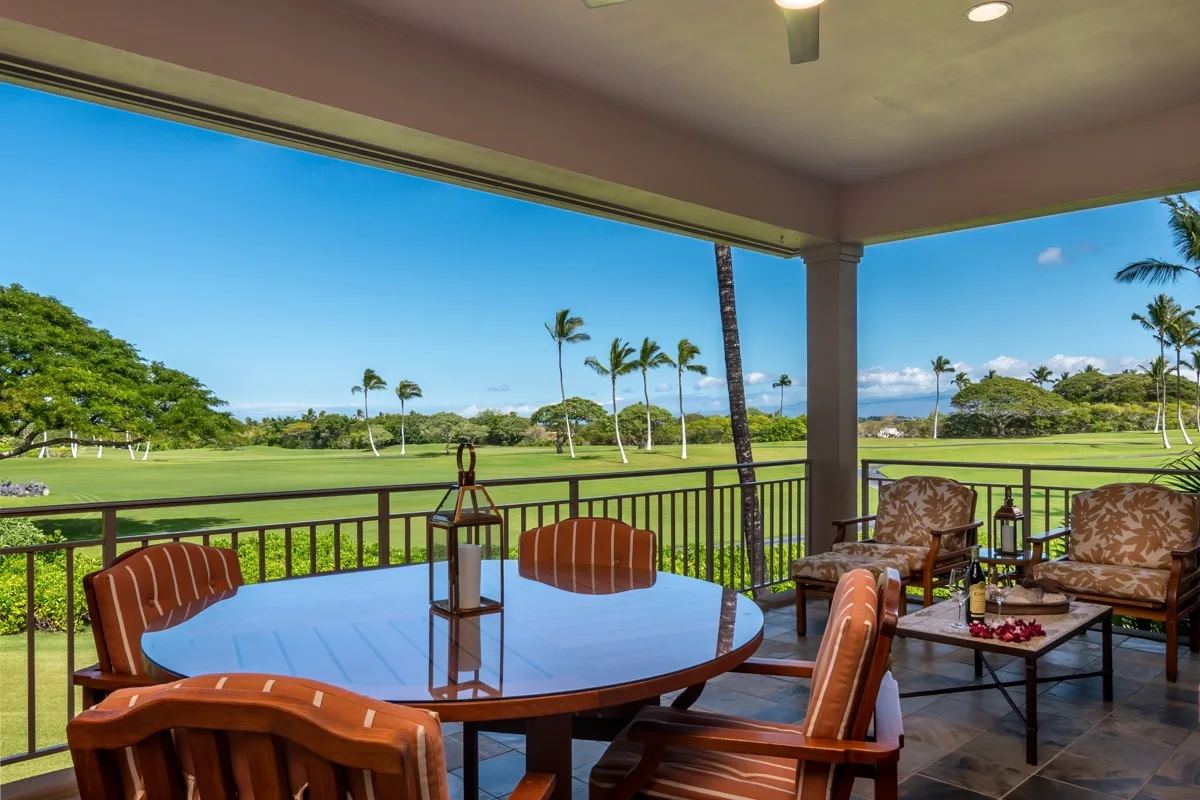 A covered patio has a round dining table and chairs overlooking a green lawn.