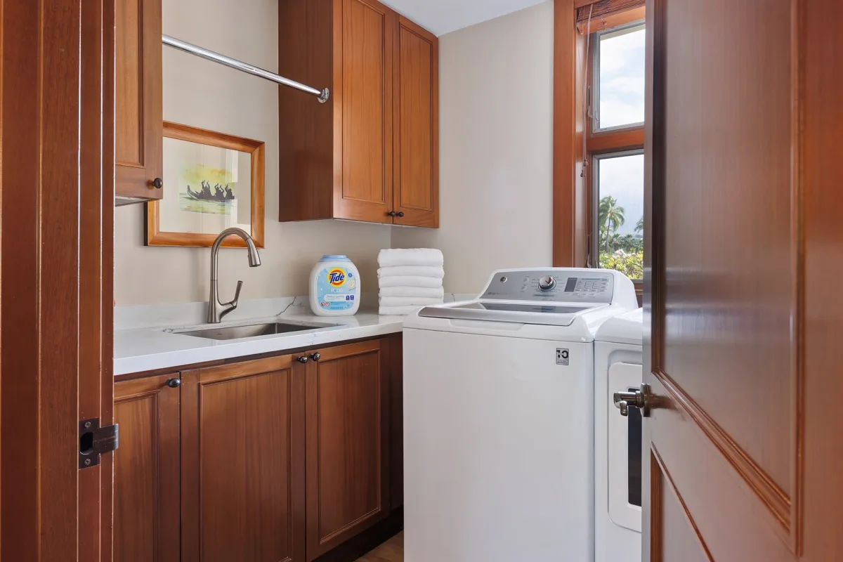 A laundry room with a washer, dryer, and sink beneath wooden cabinets.