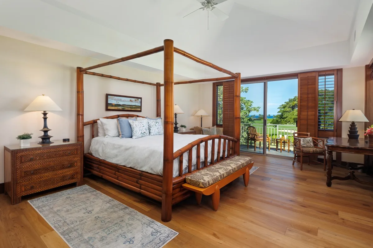 A bedroom with a wooden four-poster bed and doors opening onto a balcony.
