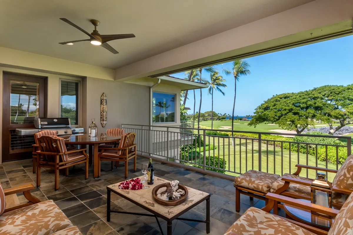A covered outdoor seating and dining area overlooks green grounds and palm trees.