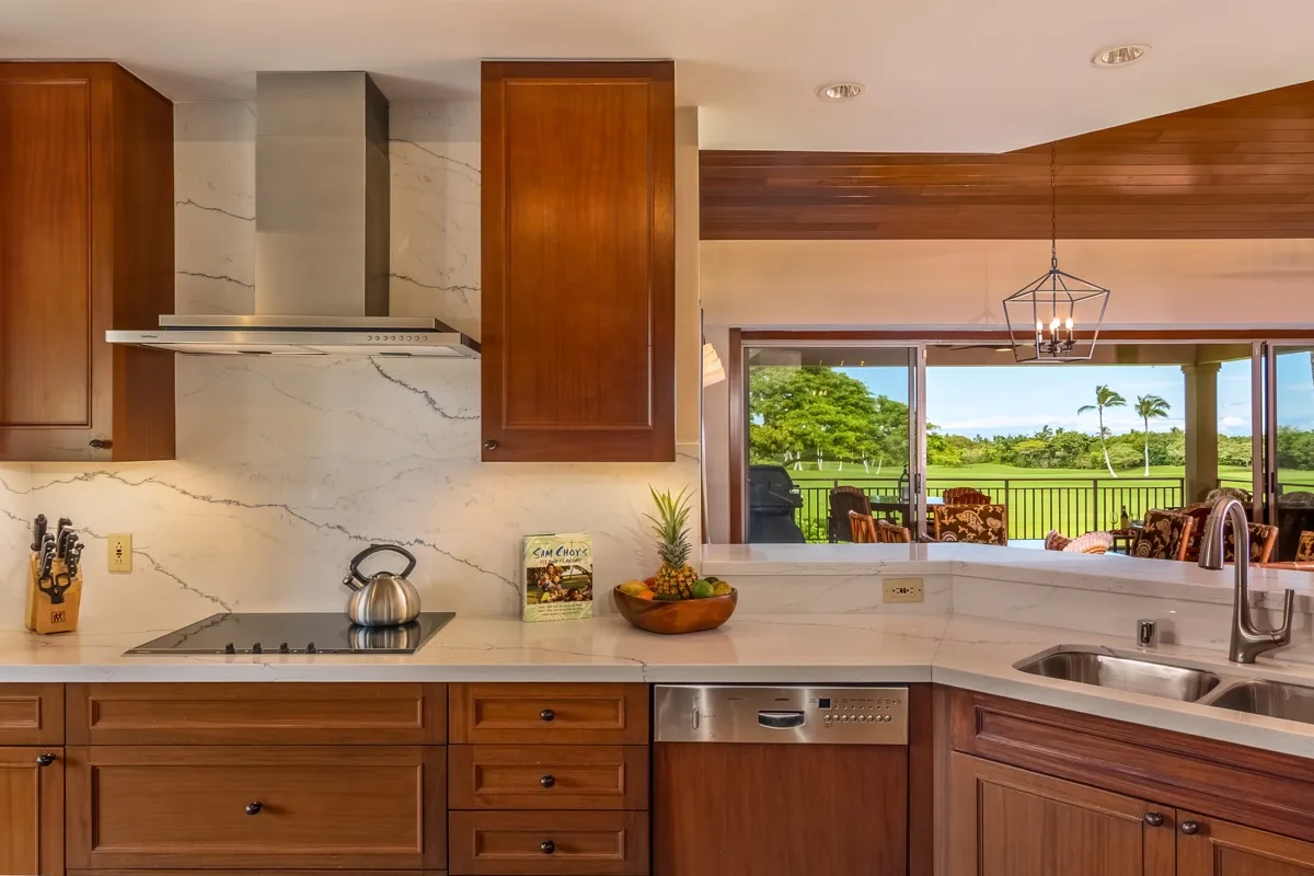 A kitchen with wooden cabinetry and a wide window overlooking a green landscape.