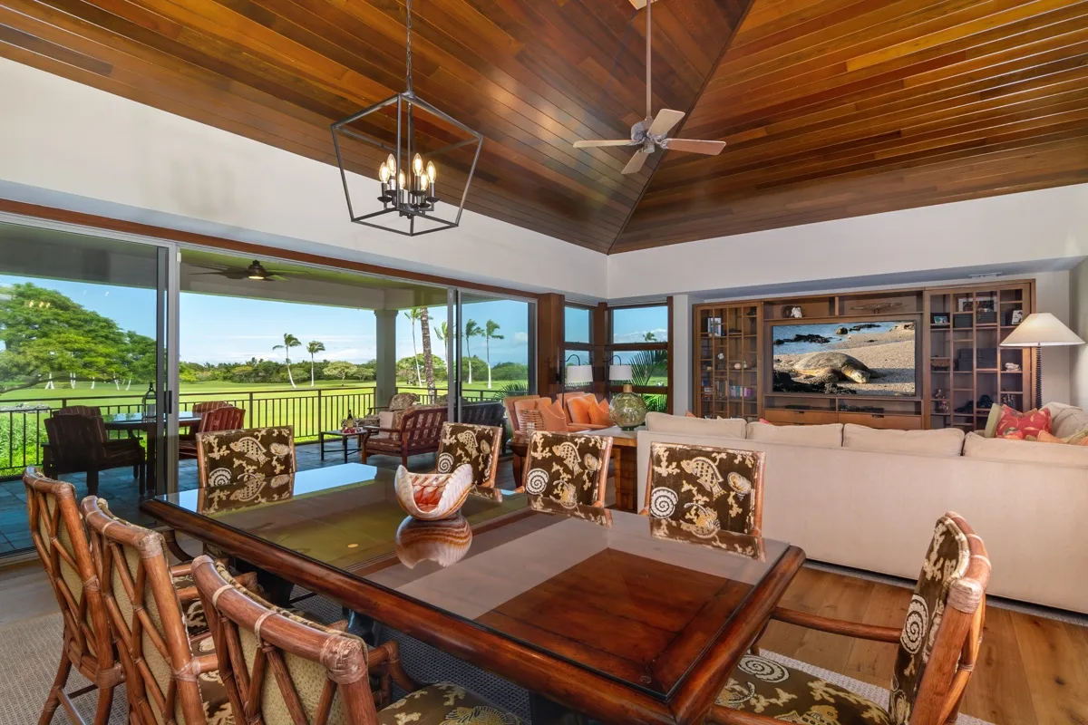 A spacious living and dining area with a high wooden ceiling and large windows.