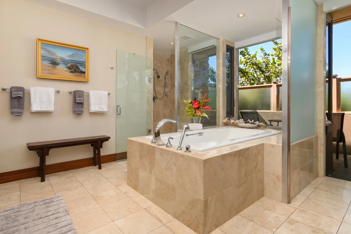 A spacious bathroom features a large bathtub, glass shower, and windows overlooking greenery.