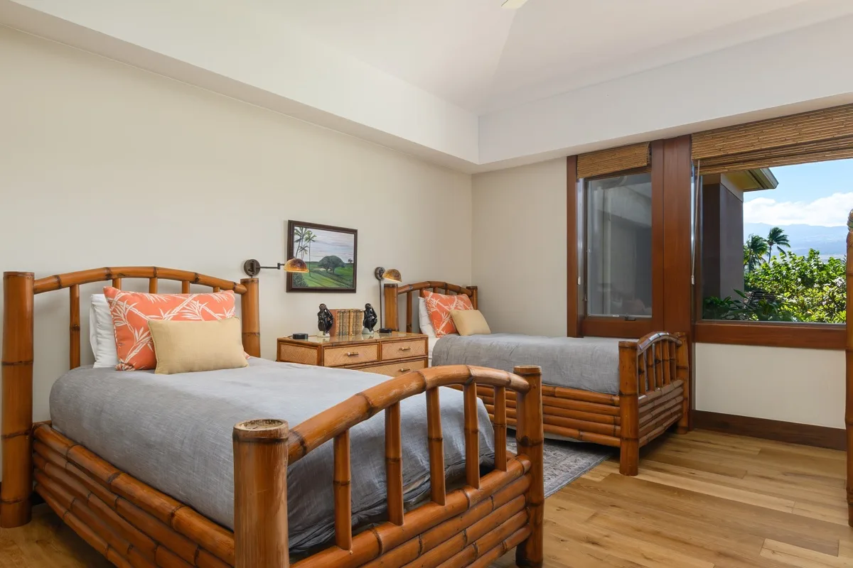 A bedroom with two beds, bedside tables, and a large window overlooking greenery.