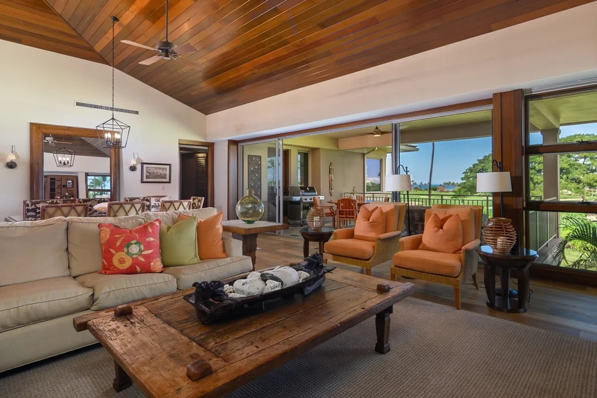 A living room with seating around a wooden coffee table and large windows.