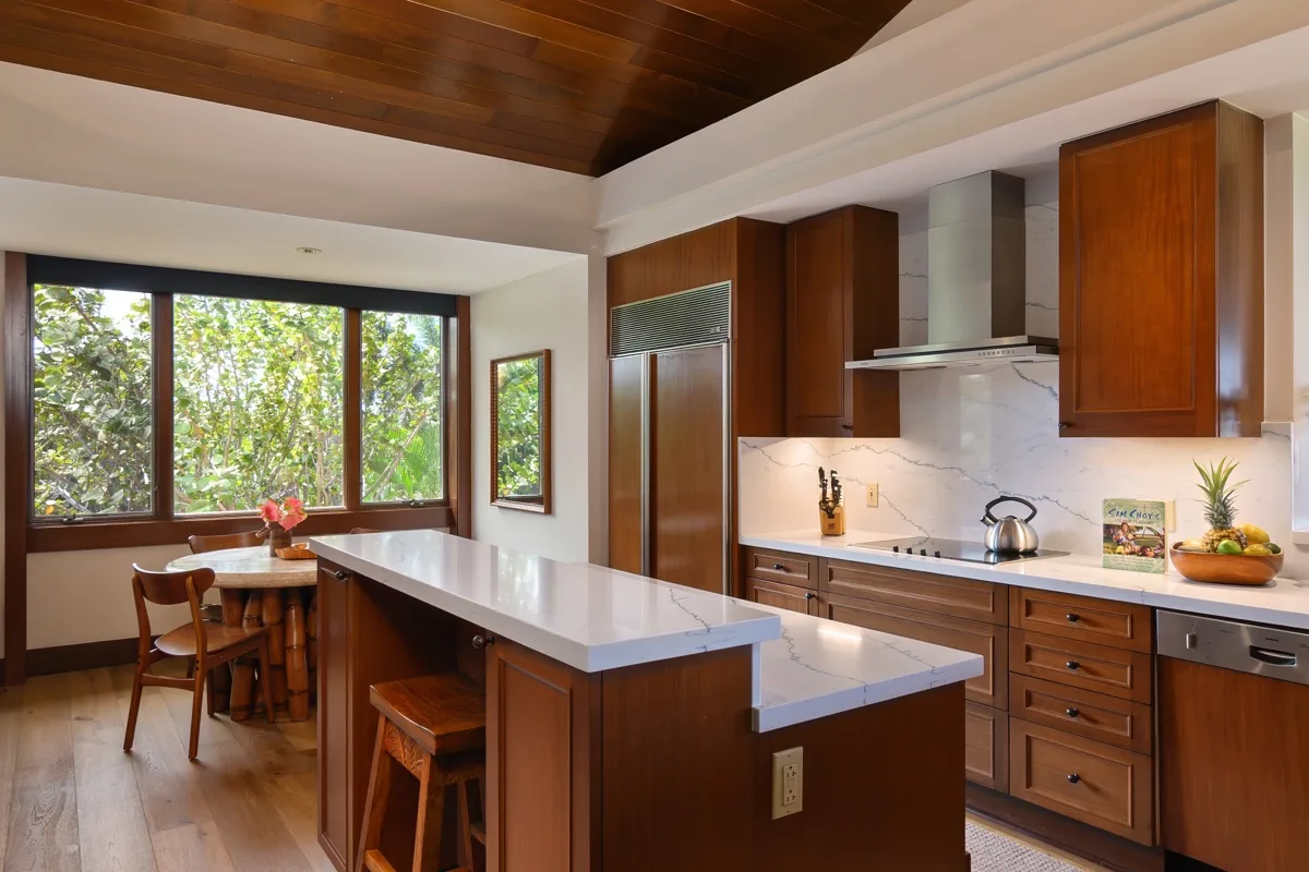 A bright kitchen with a long island, wooden cabinets, and large windows.