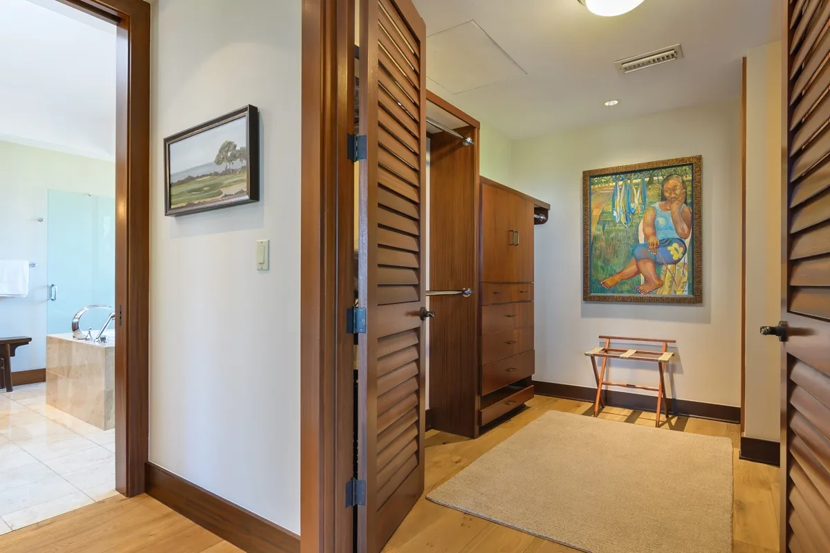 A hallway with wooden louvered doors, a rug, and framed artwork.