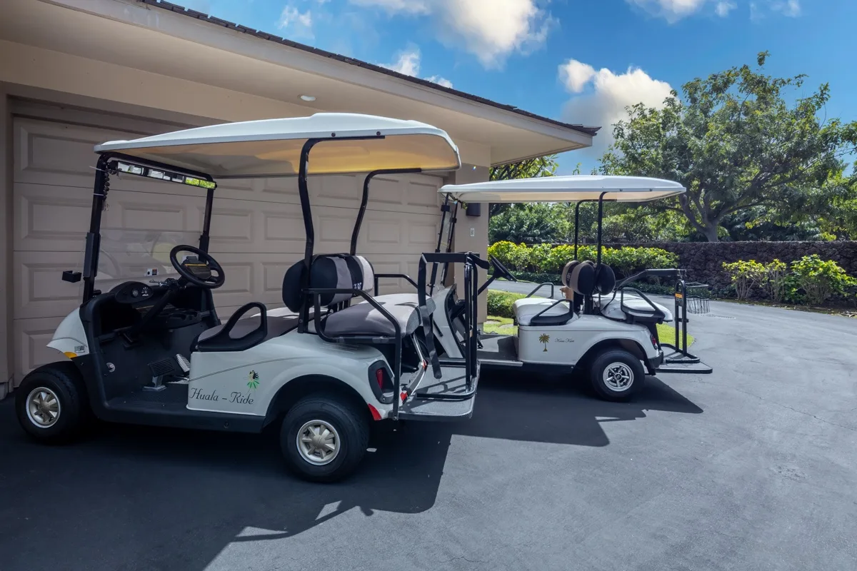 Two golf carts are parked on a paved driveway beside a garage.