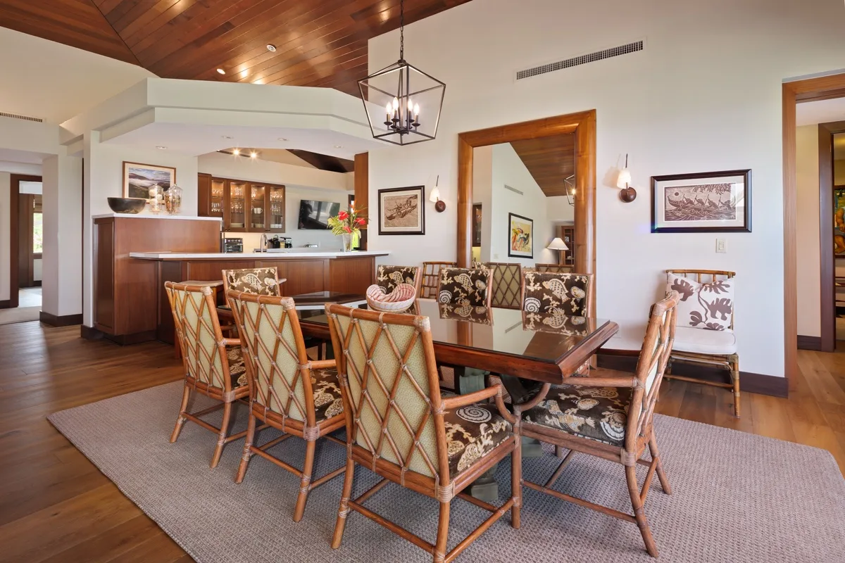 A dining area with a wooden table and patterned seating beneath a wood-paneled ceiling.