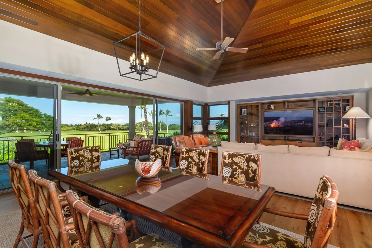 A spacious living room with a dining table, seating, and wide windows overlooking greenery.