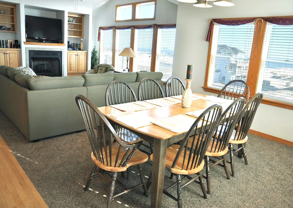 Un comedor con una mesa de madera y sillas junto a grandes ventanas.