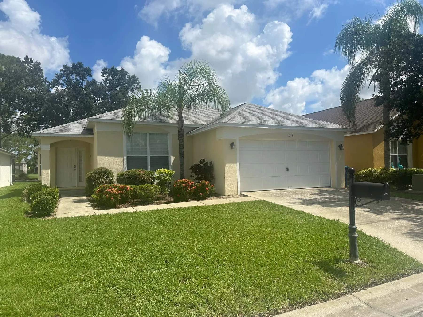 A single-story house with a garage, front lawn, and palm trees.