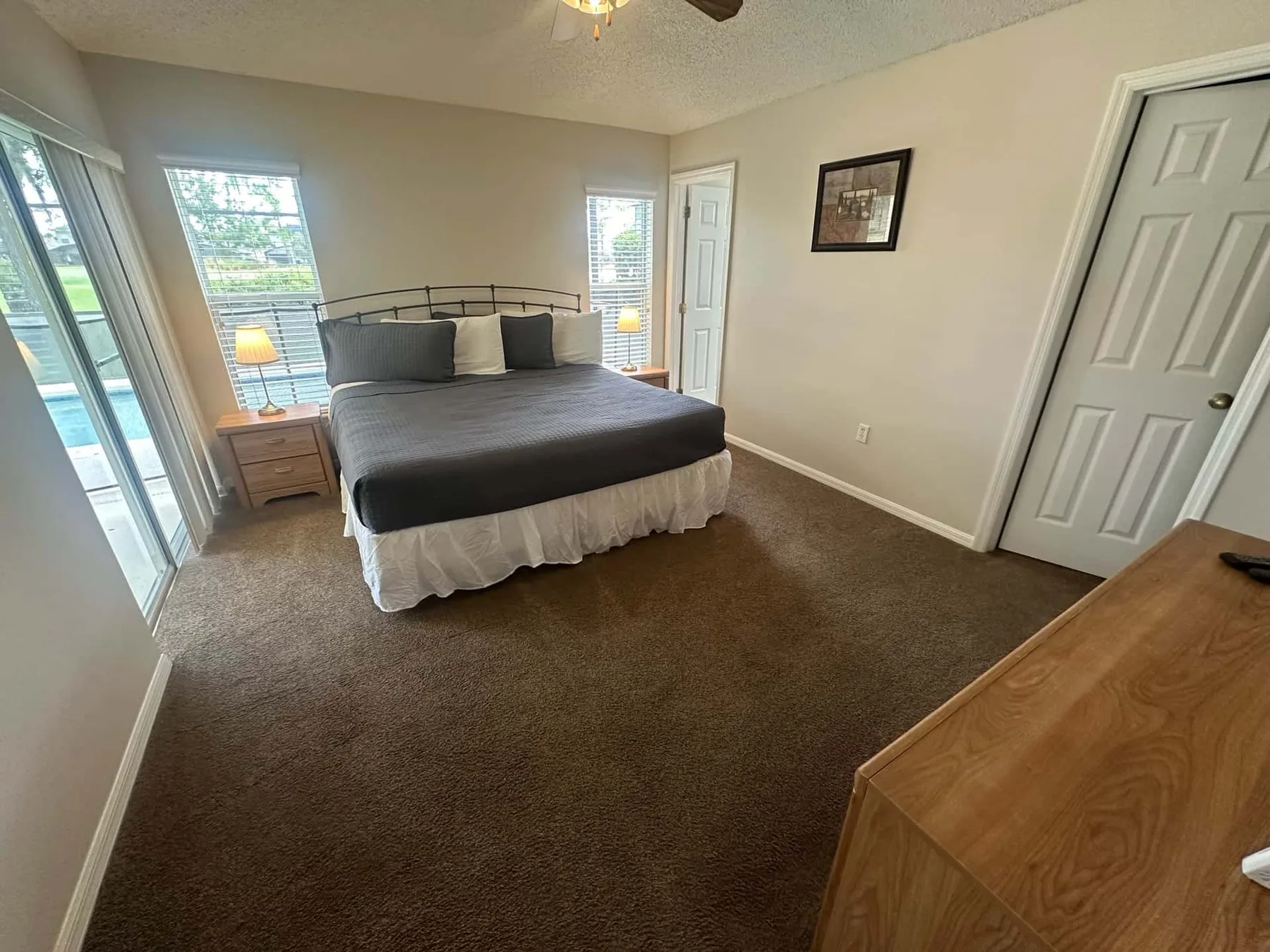Un dormitorio con una cama, mesitas de noche y ventanas con vista a zonas verdes.