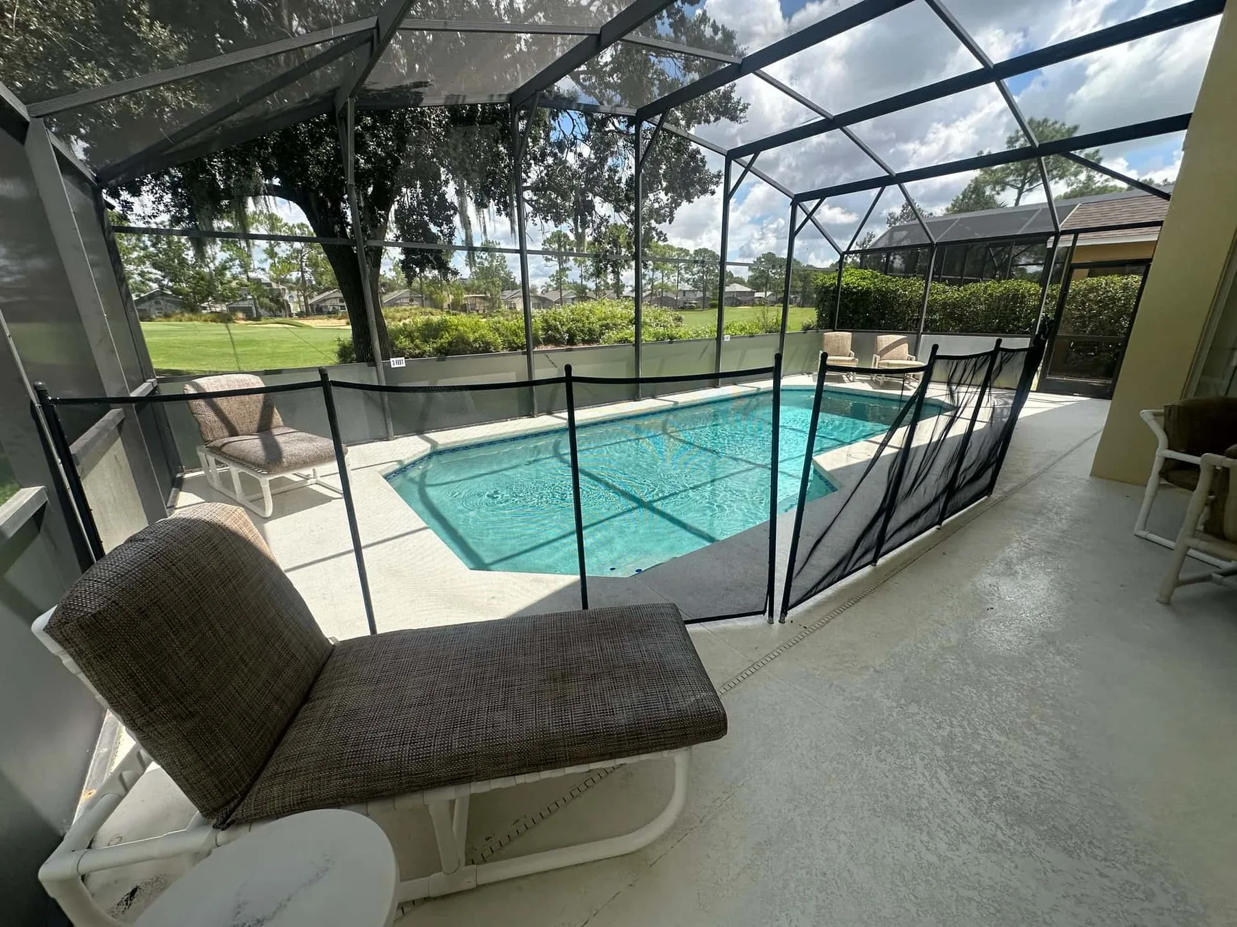 Una zona de piscina exterior con mosquitero, asientos y vistas al jardín.