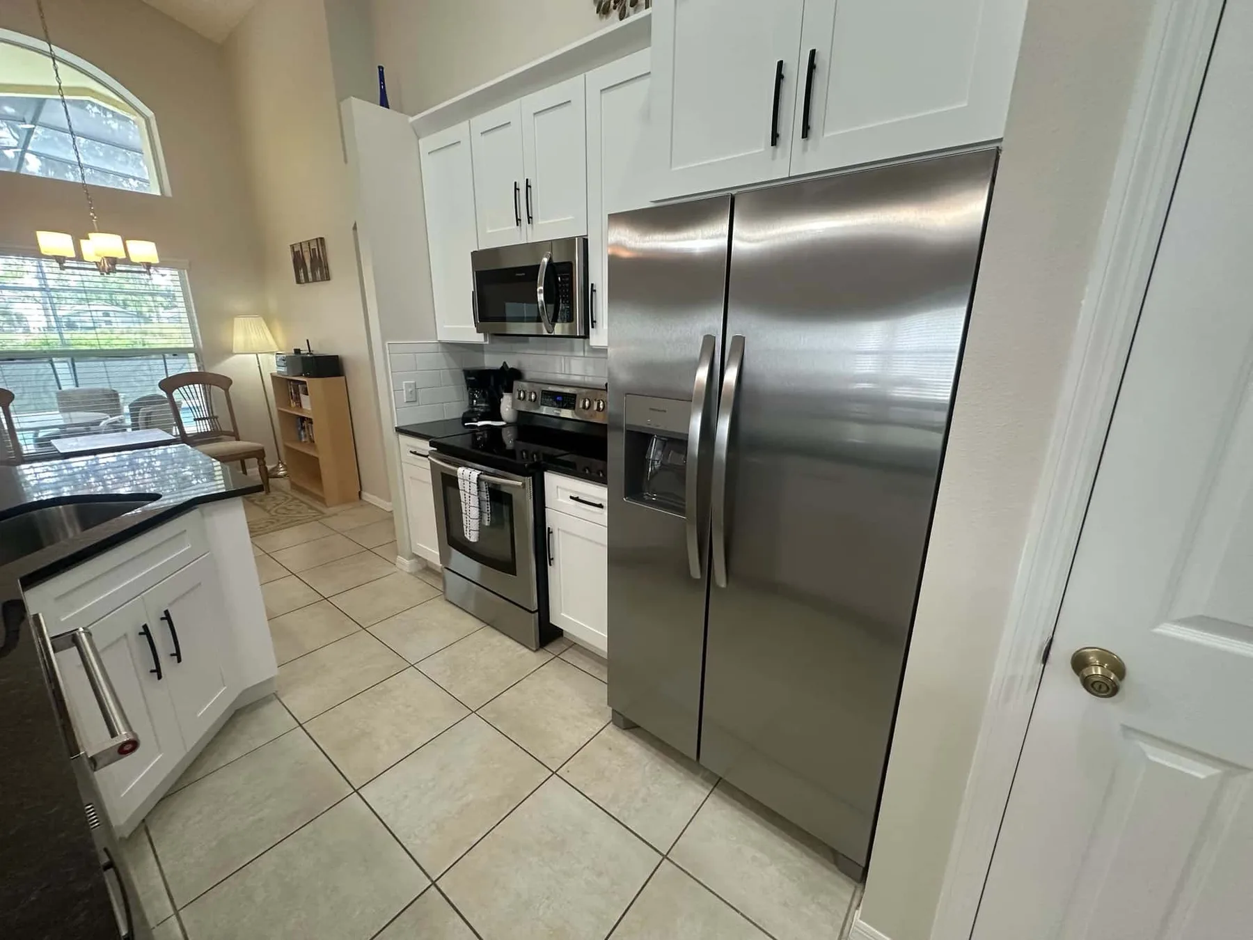 Una cocina luminosa con gabinetes blancos, electrodomésticos de acero inoxidable y piso de baldosas.