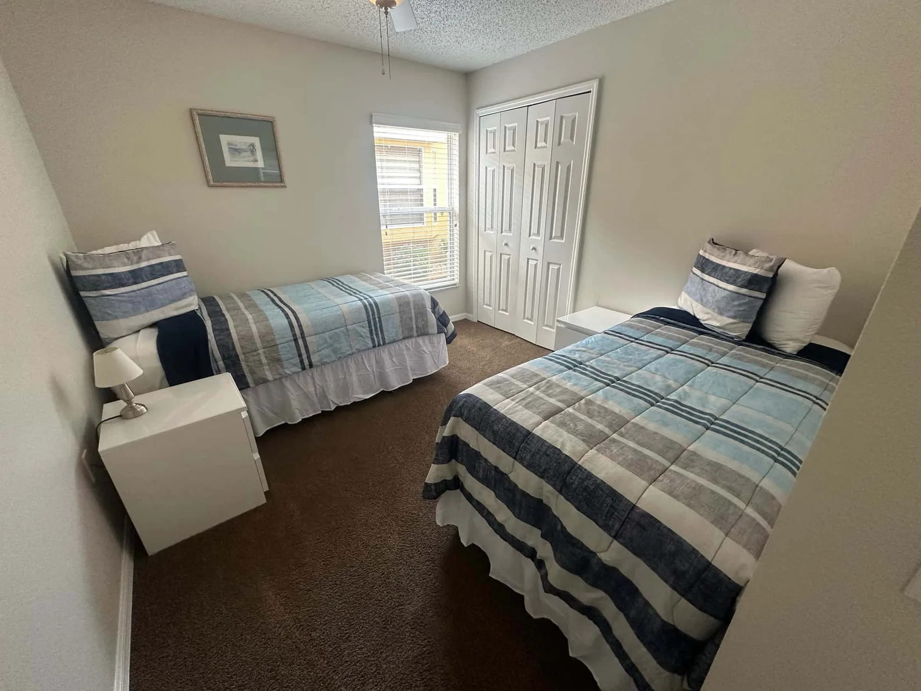 Un dormitorio con dos camas vestidas con ropa de cama a rayas azules y grises.