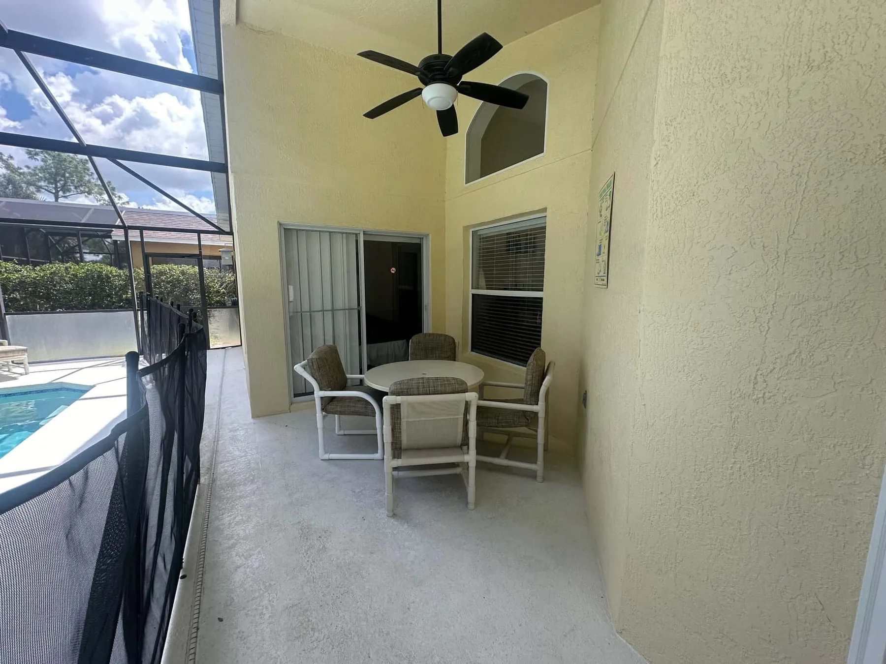 Un patio cubierto tiene una mesa redonda y asientos junto a una piscina con mosquitero.