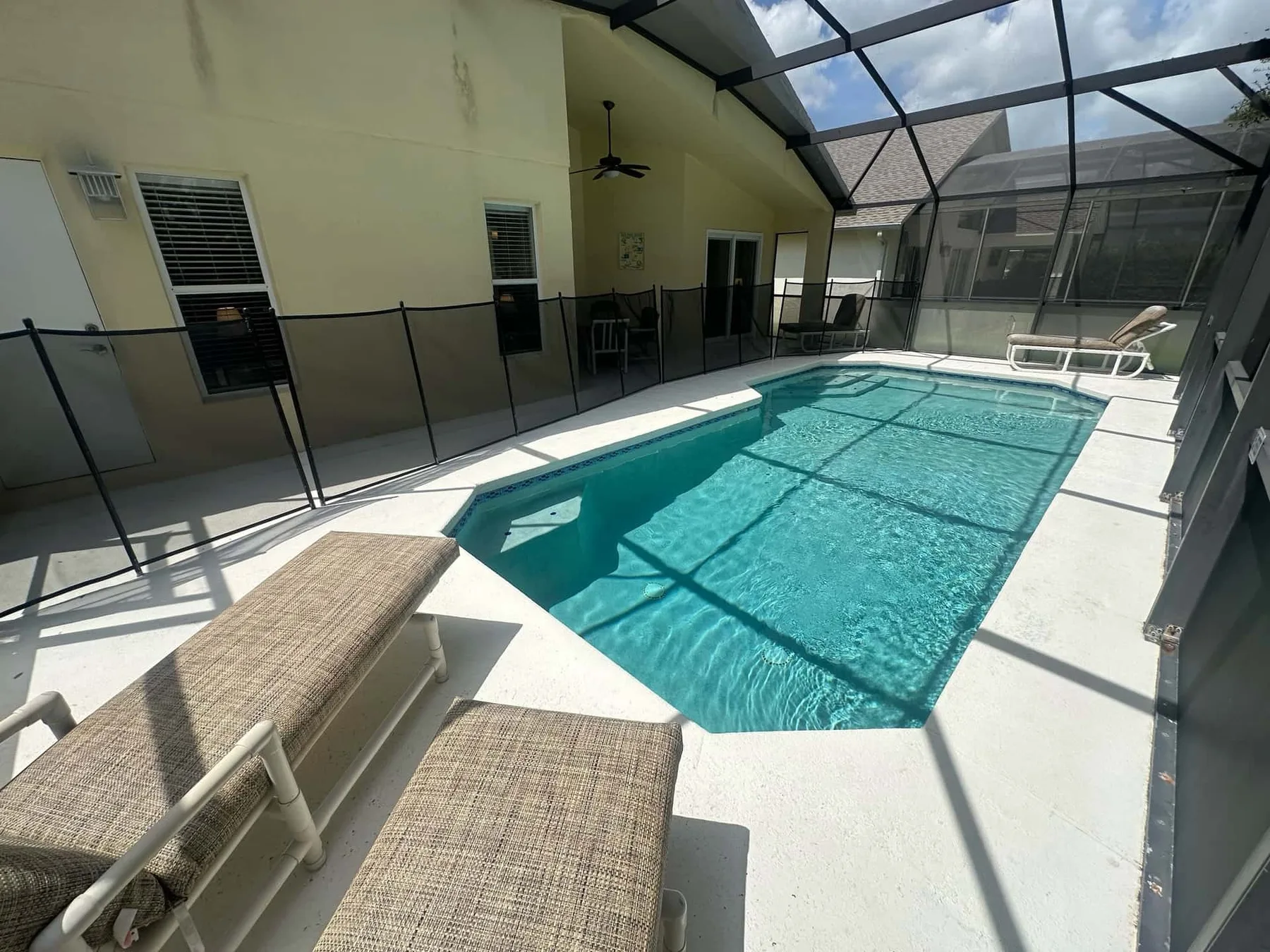 Una piscina está en un patio con mosquitero junto a una casa.