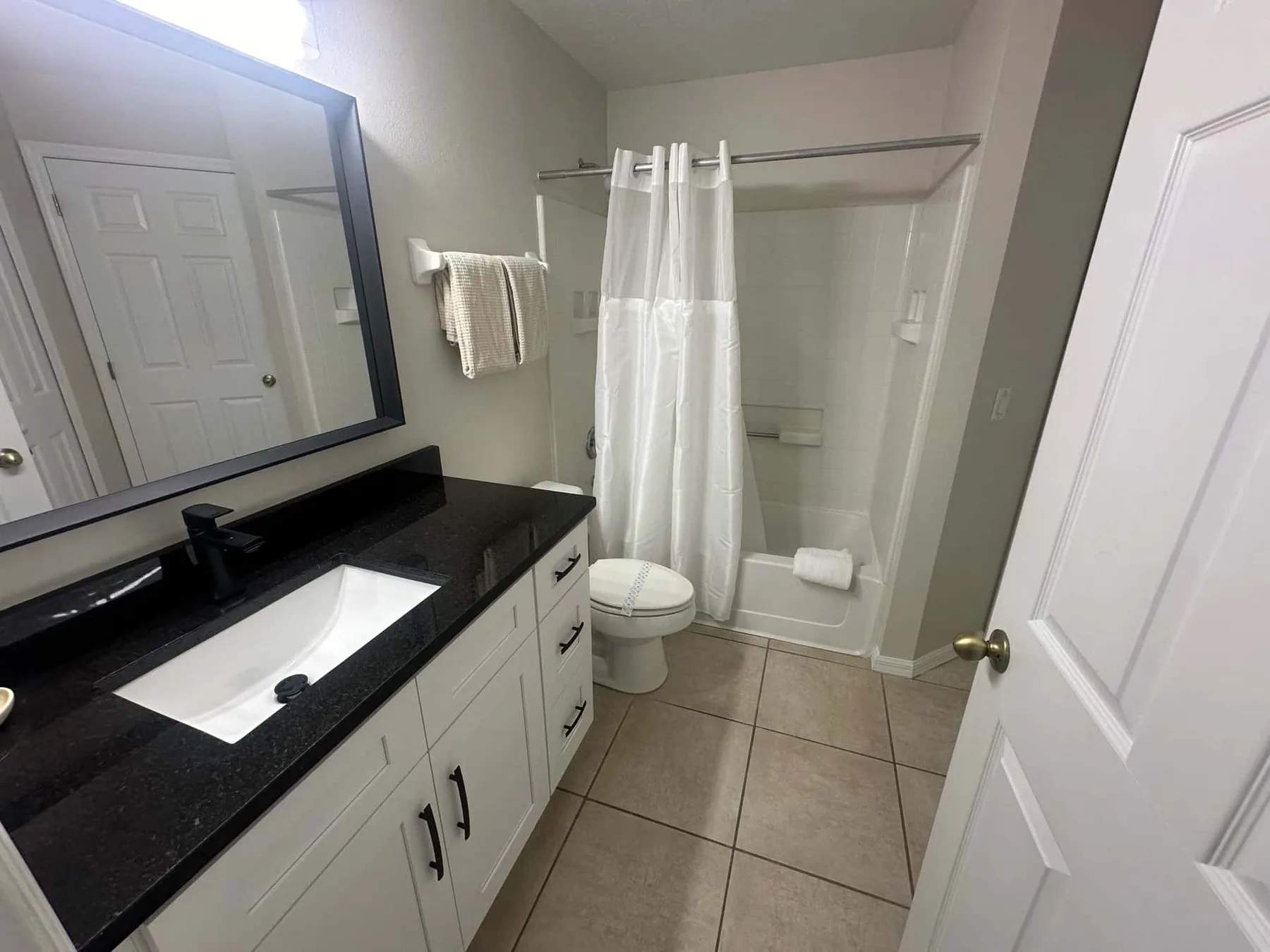 Un baño con una encimera oscura, lavabo, inodoro y cortina de ducha.