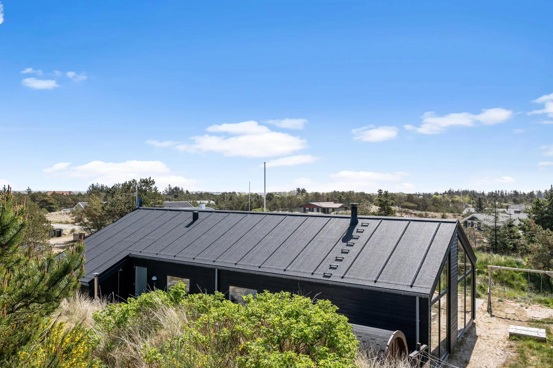 Una casa moderna oscura está entre arbustos bajos bajo un cielo azul despejado.
