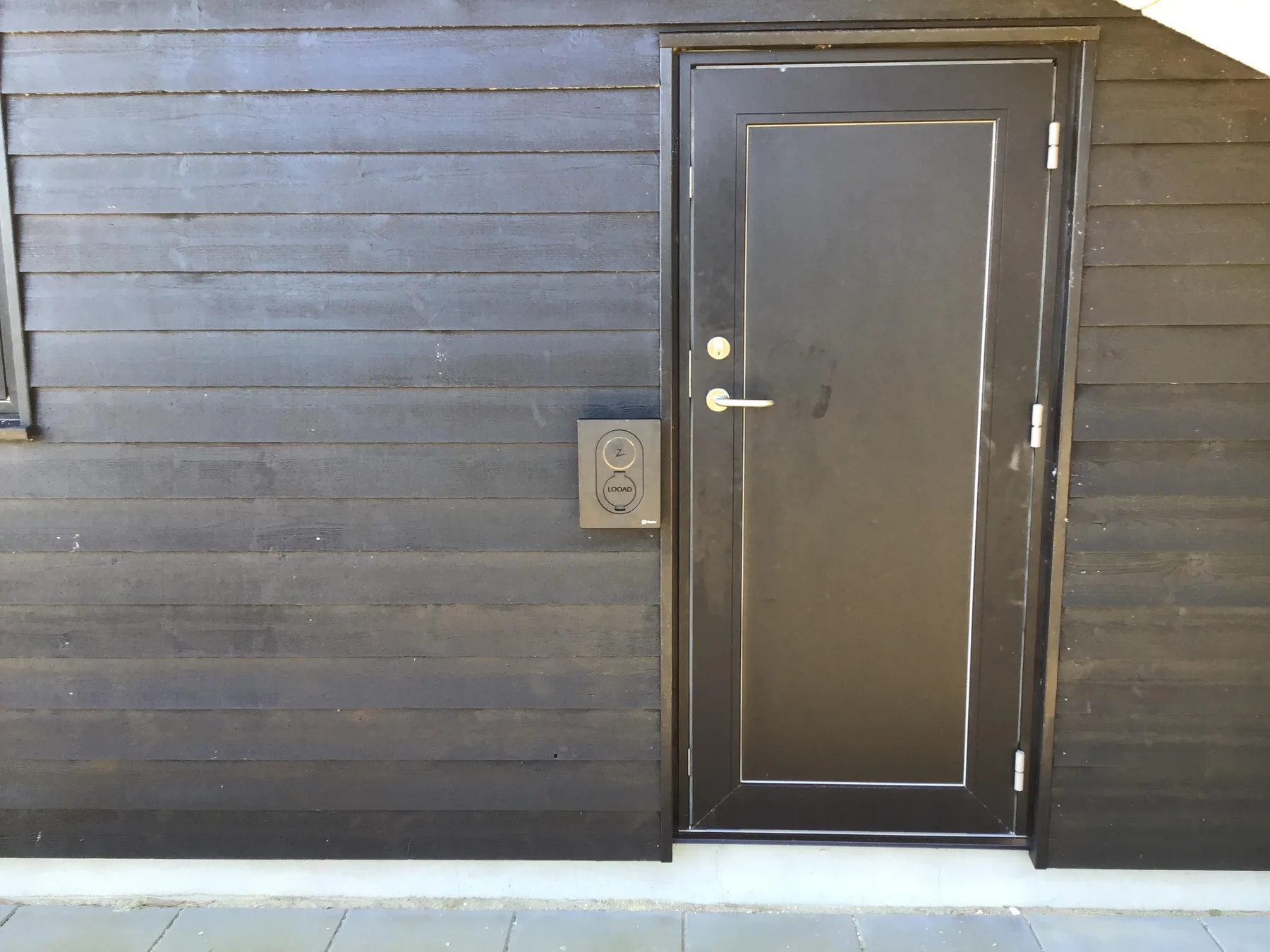 Una entrada exterior con una puerta oscura en un revestimiento horizontal.